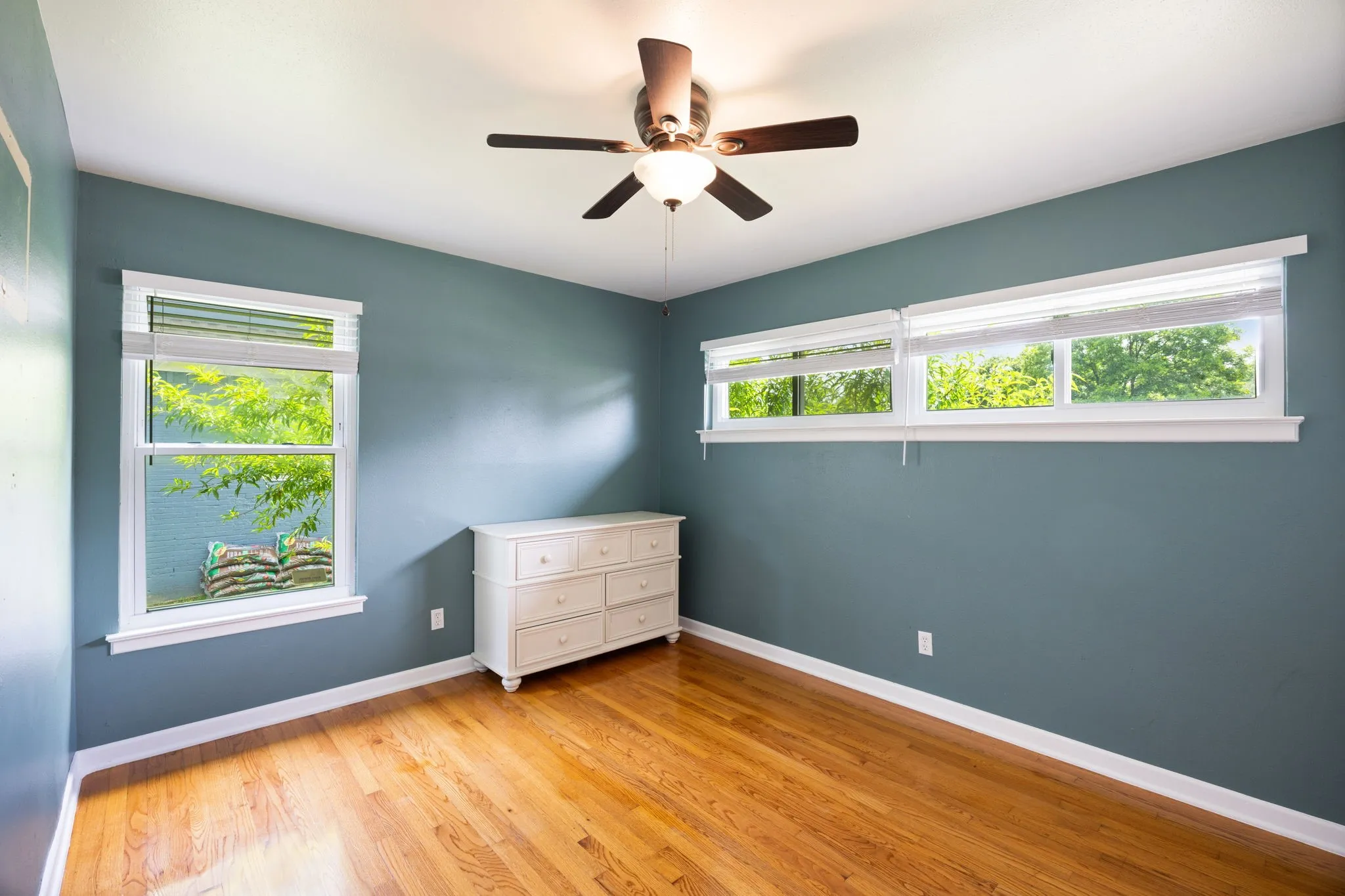 Wood-finish flooring, white window trim, and a ceiling fan with integrated lighting