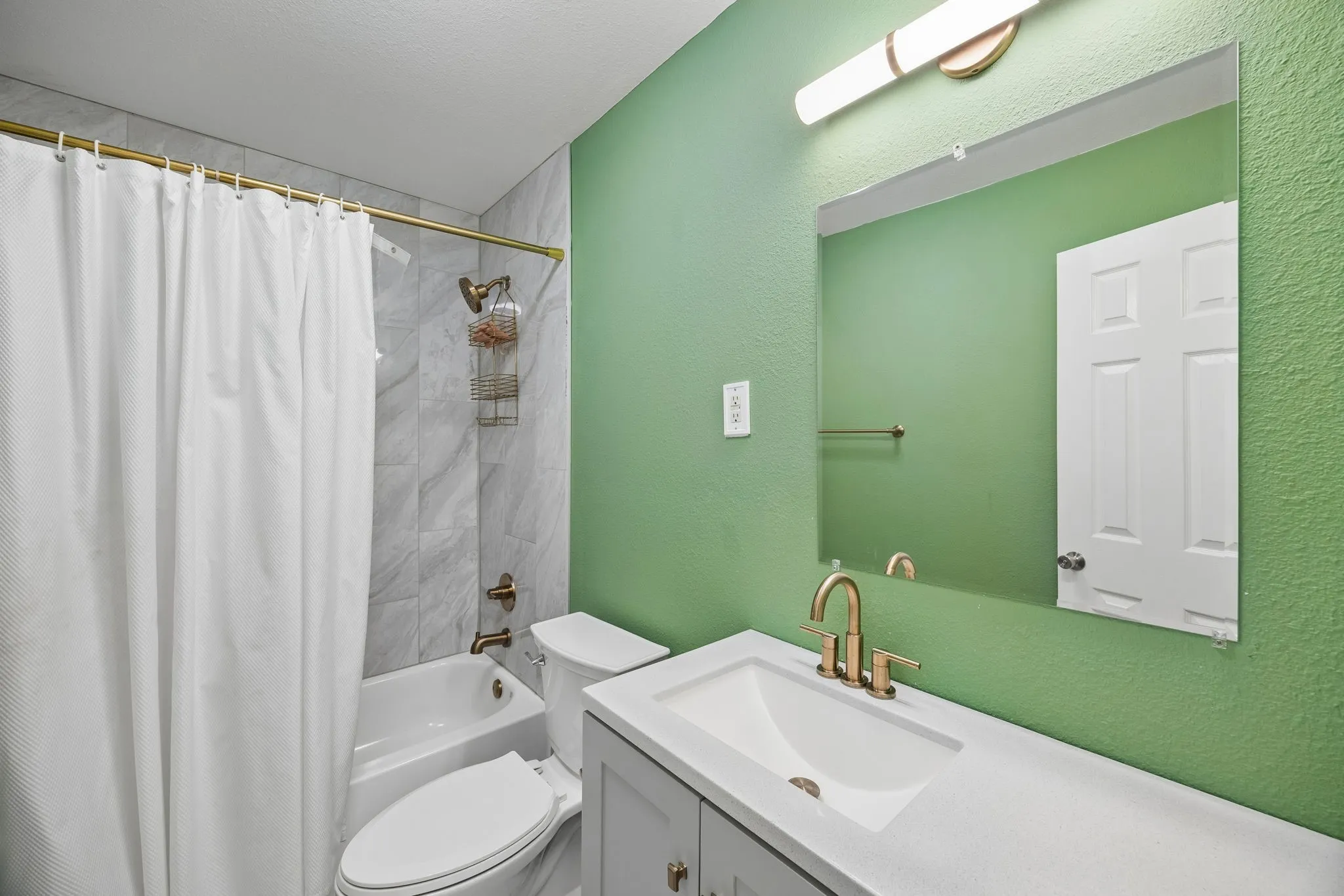 Bathroom with light gray vanity, white countertop, rectangular undermount sink, and brass-finish fixtures