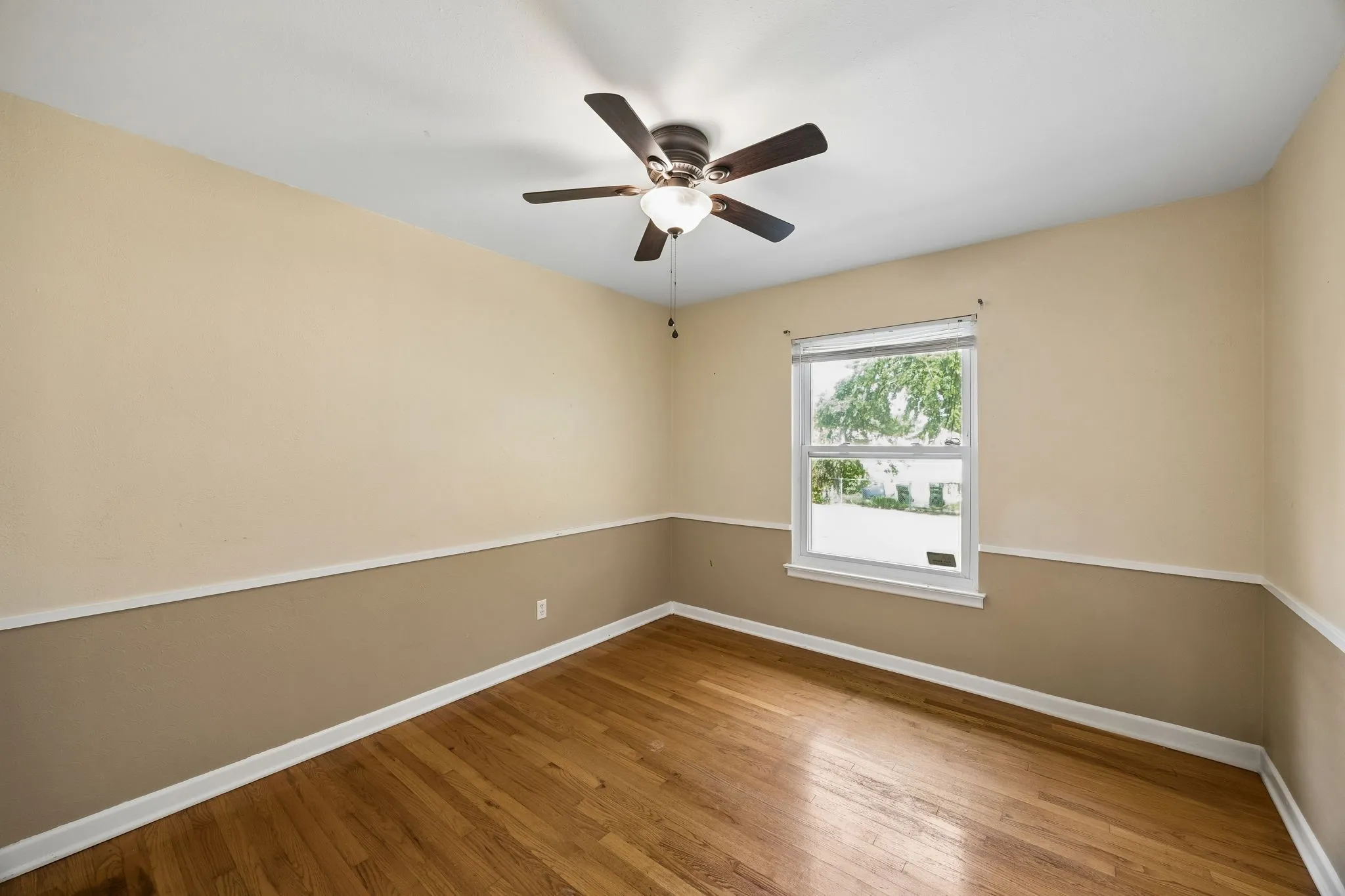 Hardwood flooring, painted walls with chair rail molding, ceiling fan with integrated lighting, and a single window