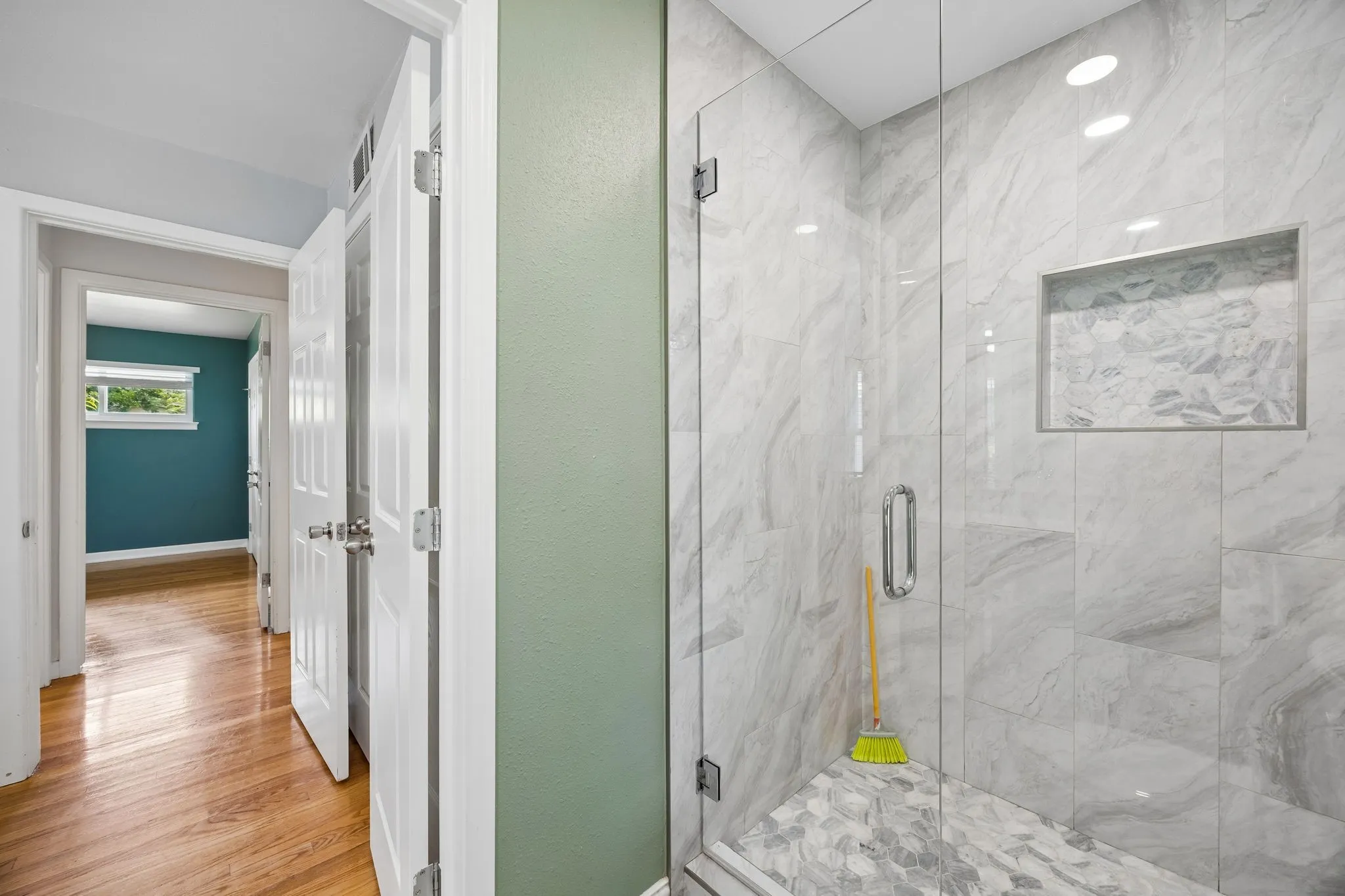 Glass-enclosed shower with large format wall tile, recessed shower niche, and mosaic tile flooring
