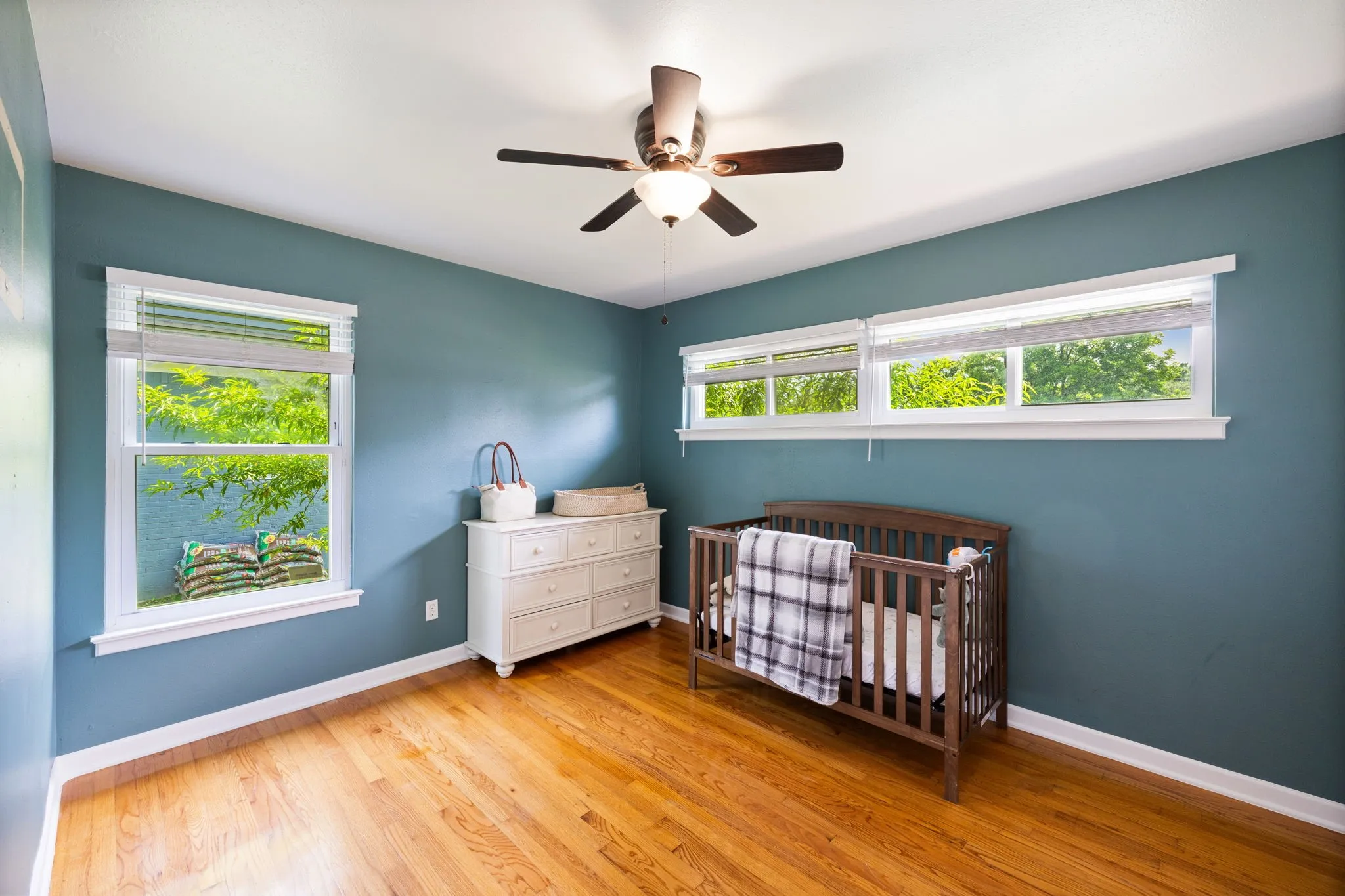Hardwood flooring, multiple windows with white trim, ceiling fan with integrated lighting, white baseboards, and painted walls
