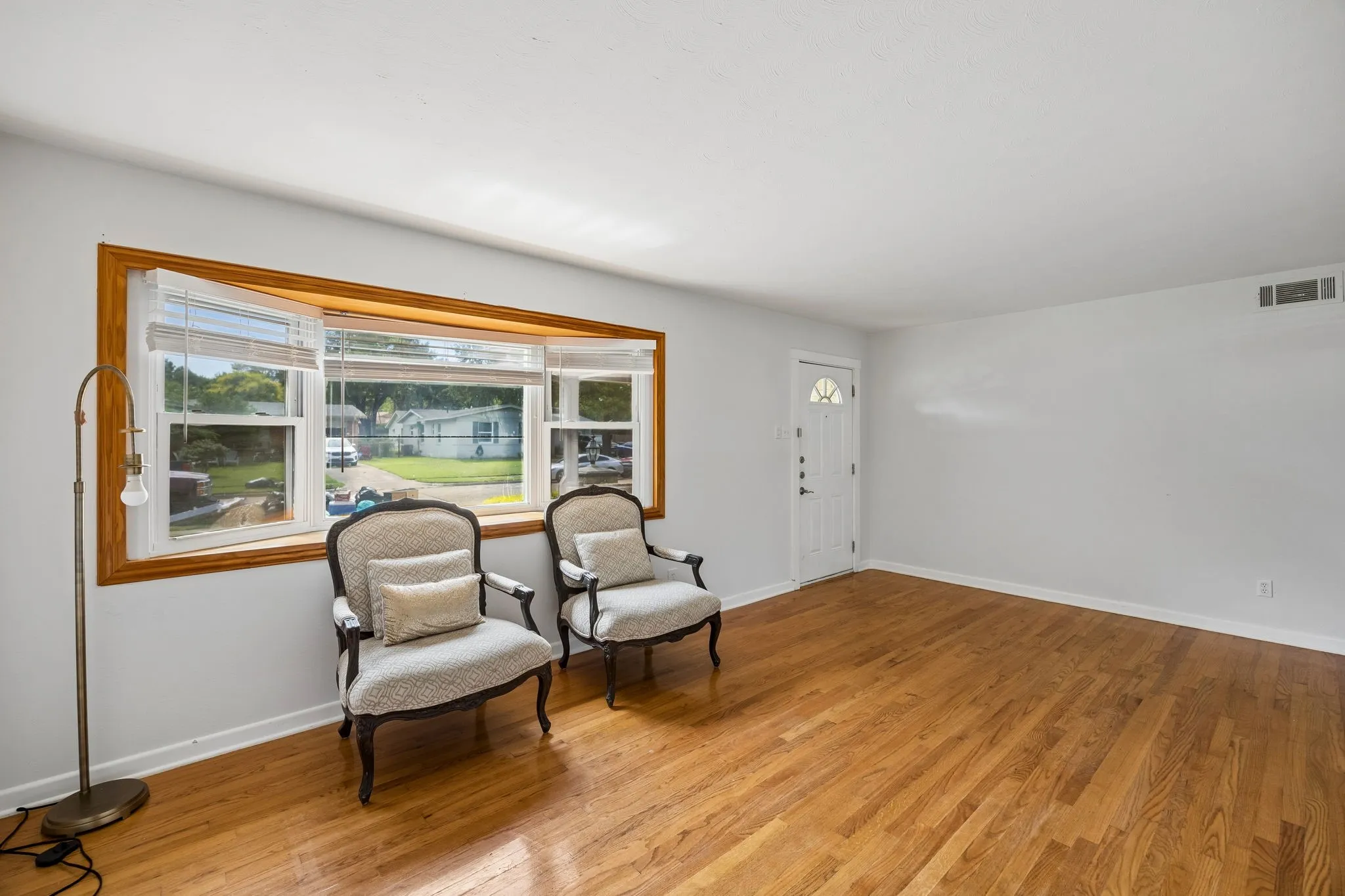 Hardwood flooring, bay window with wood trim, white walls, and a paneled entry door with an arched window