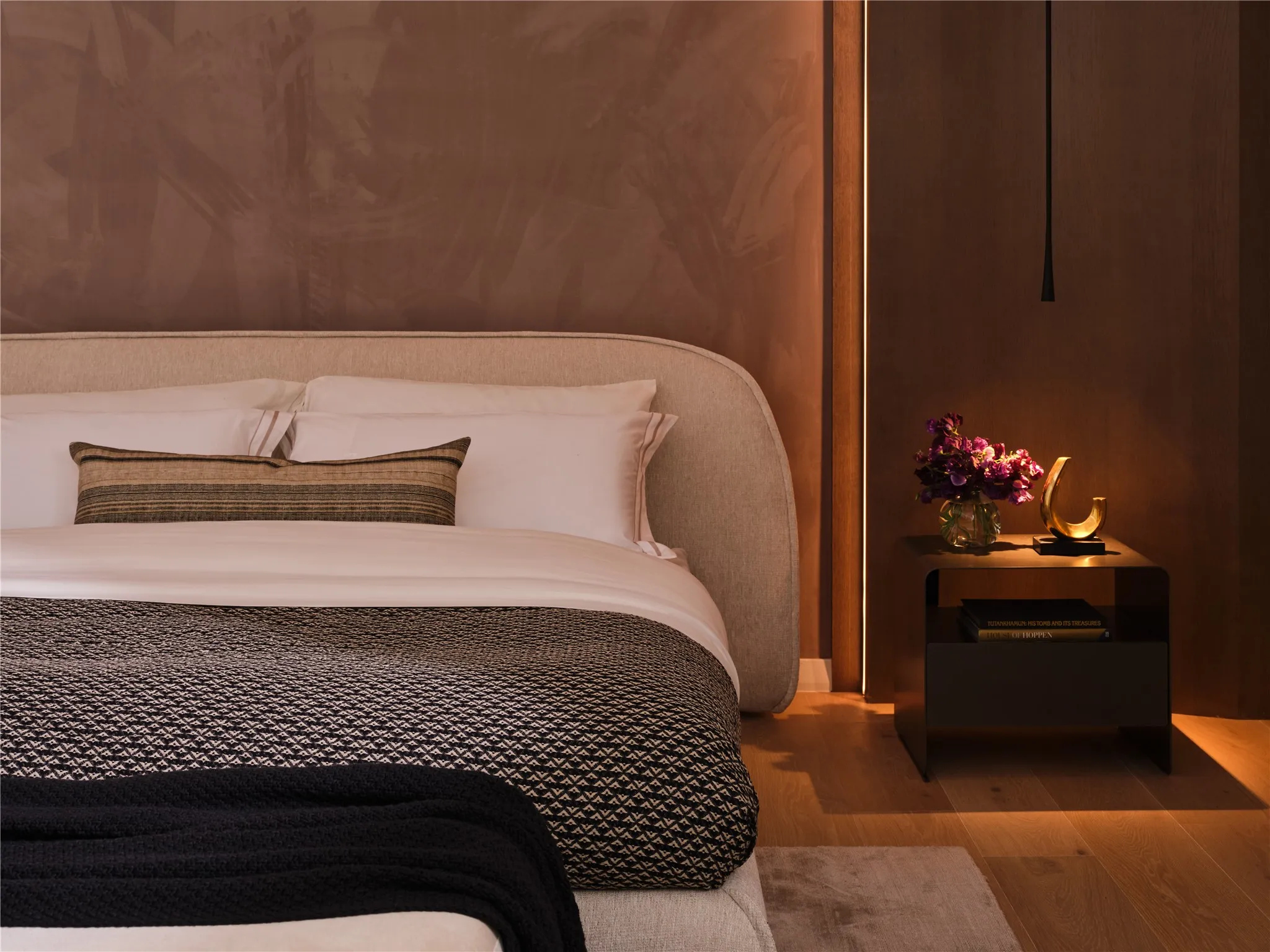 Primary Bedroom highlights include Phillip Jeffries® velvet accent wall and curved rift-cut white oak paneling and pendant lighting.