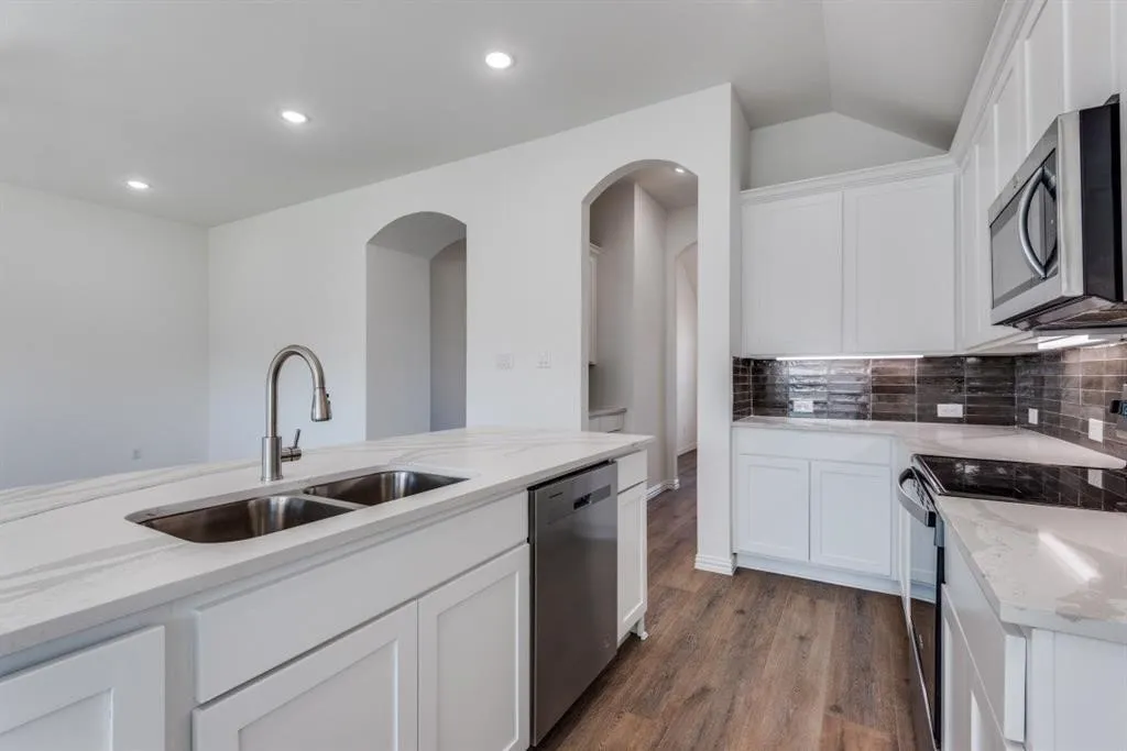 Kitchen featuring white cabinetry, stainless steel appliances, stone-finish countertops, wood-finish flooring, and arched doorways