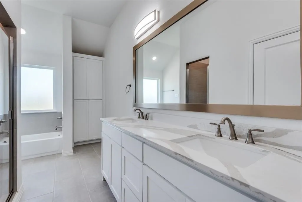 Double vanity with undermount sinks, stone countertops, large framed mirror, built-in storage cabinetry, and a bathtub with tiled surround