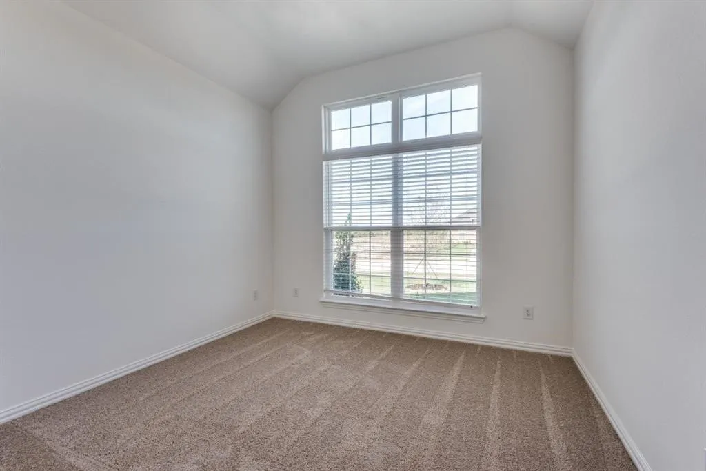 Vaulted ceiling, neutral tone walls, large window with horizontal blinds, tan carpet flooring
