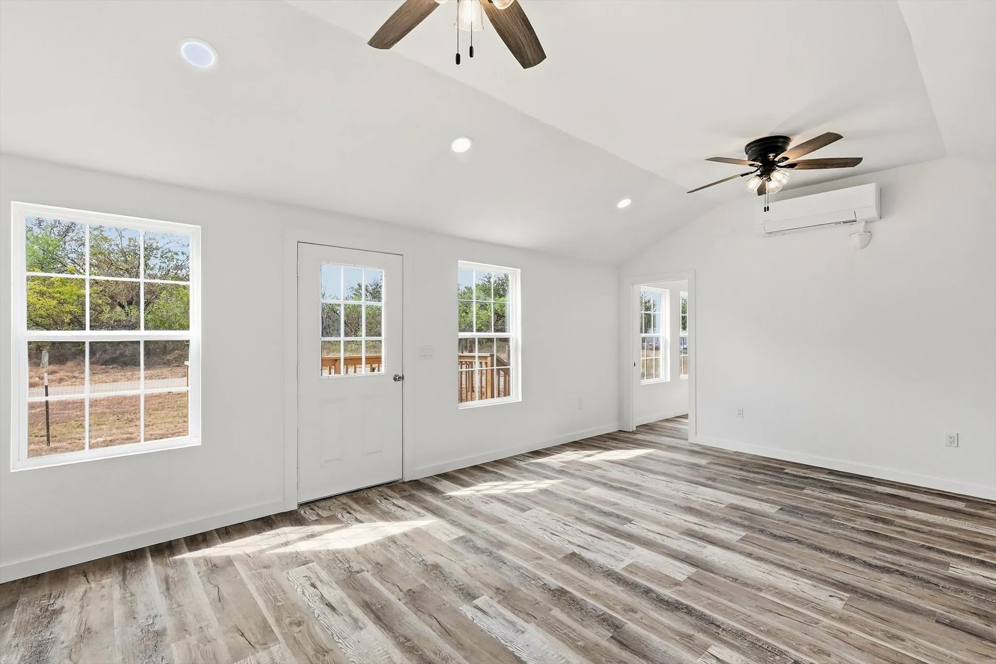 Vaulted ceiling with dual ceiling fans, recessed lighting, wood-finish flooring, and multiple windows