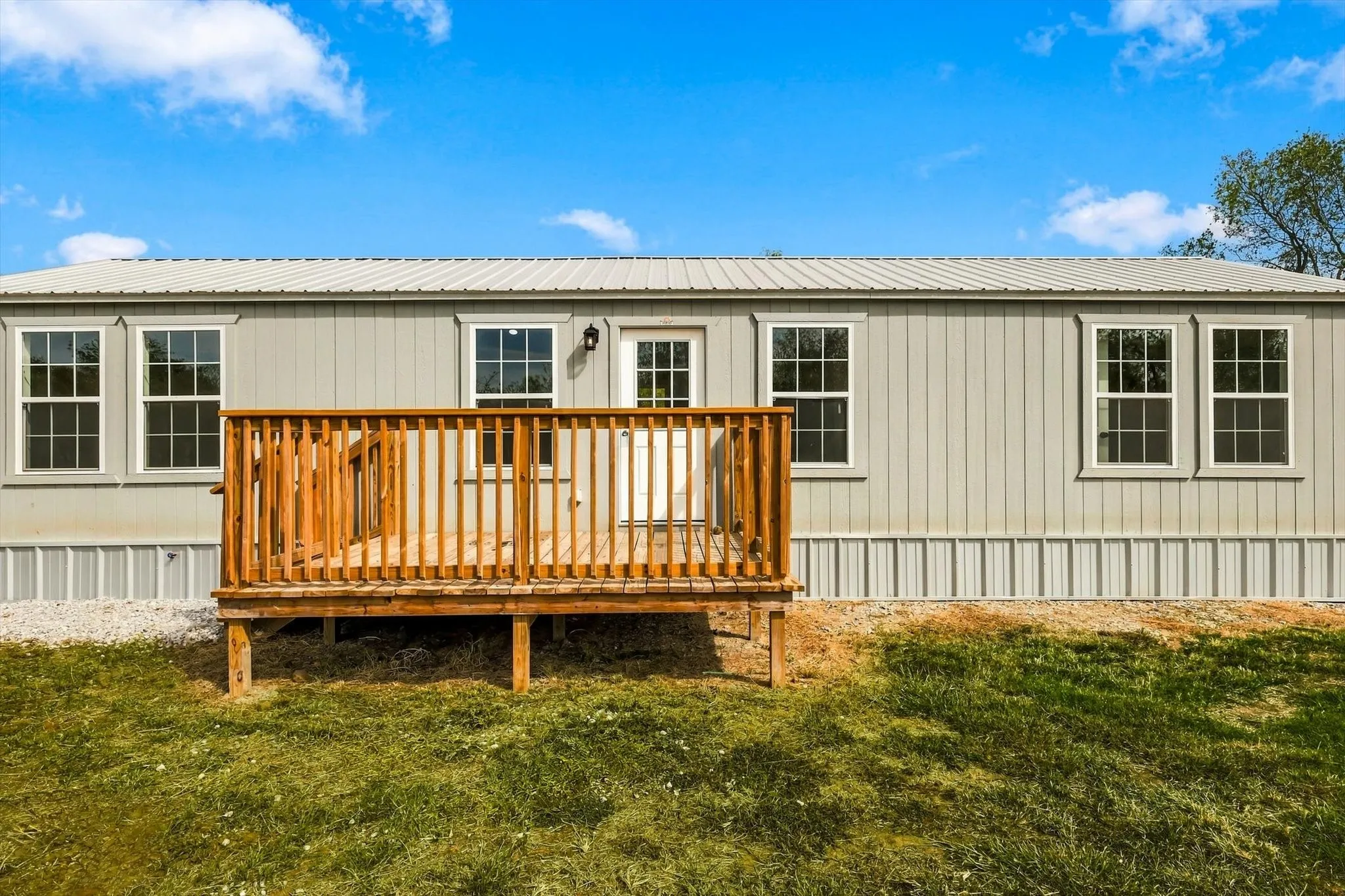 Exterior featuring a metal roof, light-colored siding, multiple pane-style windows, and a wood-finish deck