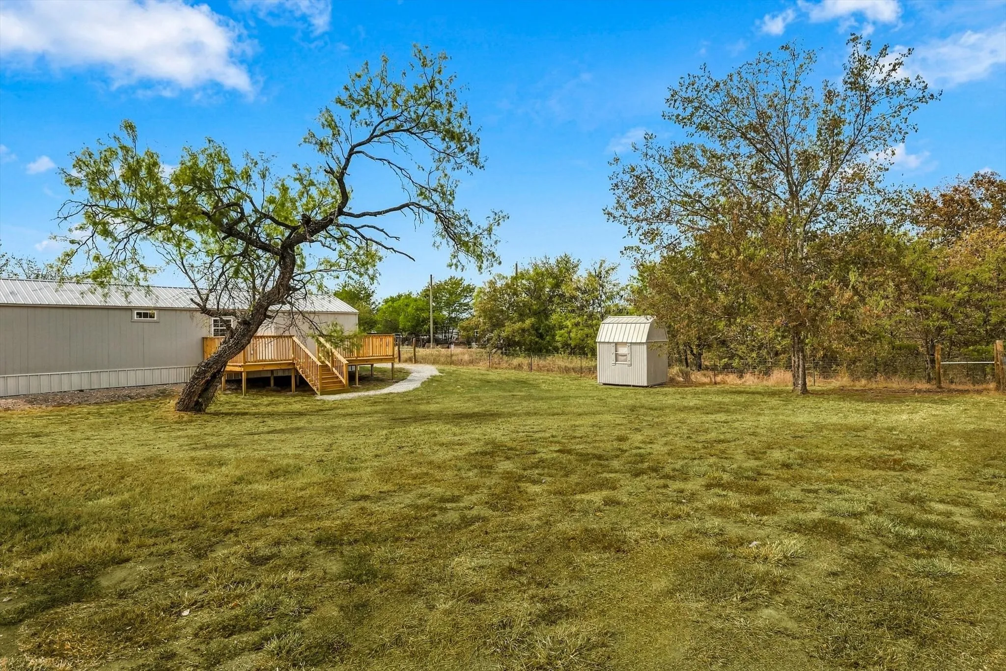 Expansive grassy area backyard with a wooden deck featuring railings, a small shed, and mature trees