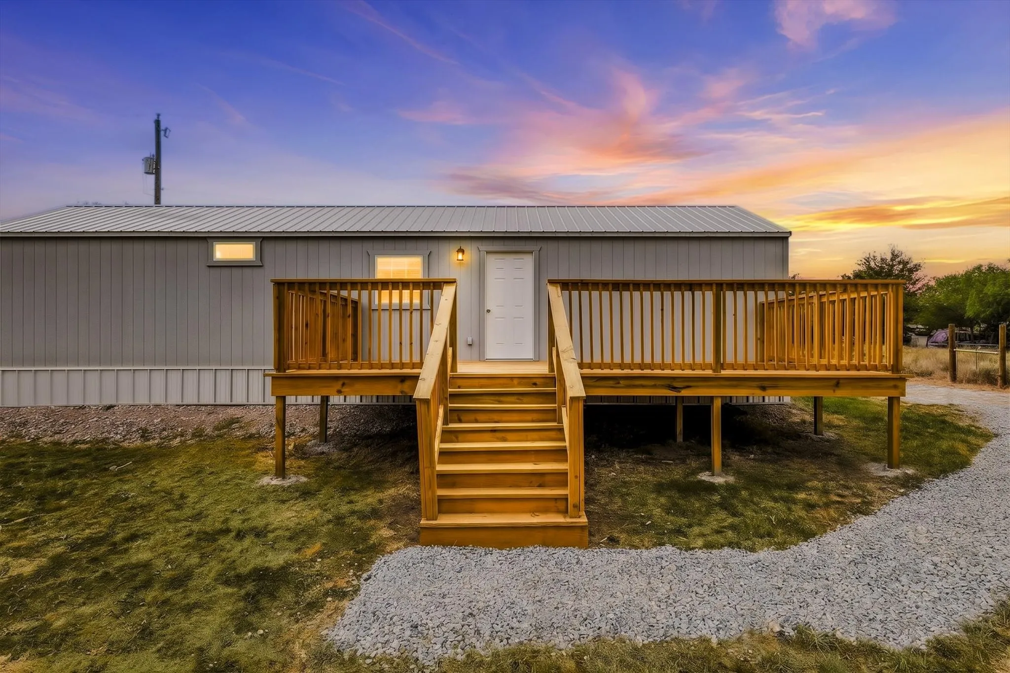 Expansive wood-finish deck with railings, exterior lighting, and a gravel pathway