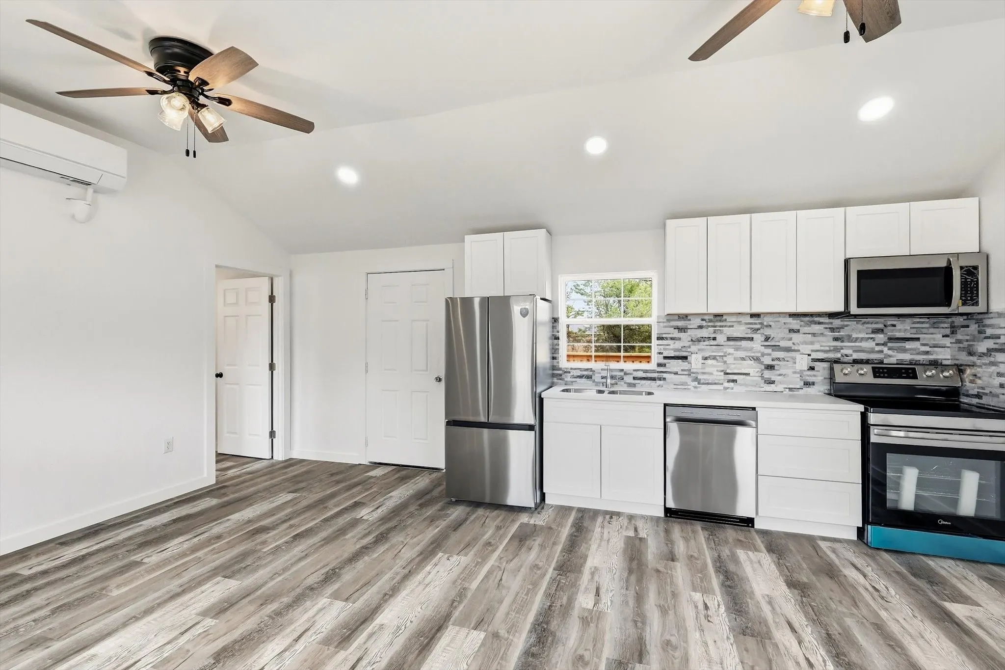 Vaulted ceiling, wood-finish flooring, recessed lighting, stainless steel appliances, and white cabinetry