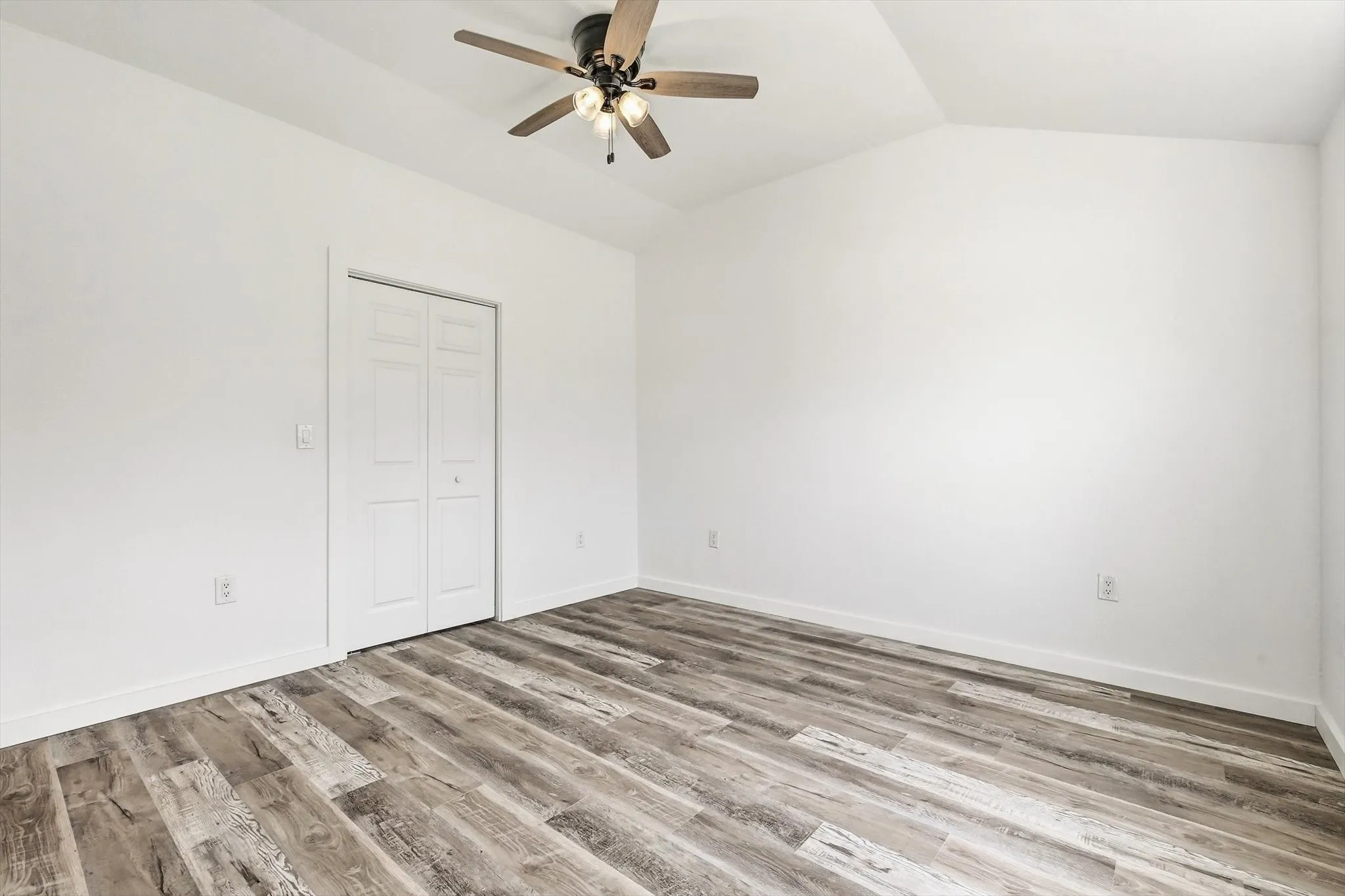 Vaulted ceiling with a ceiling fan, wood-finish flooring, and bi-fold closet doors