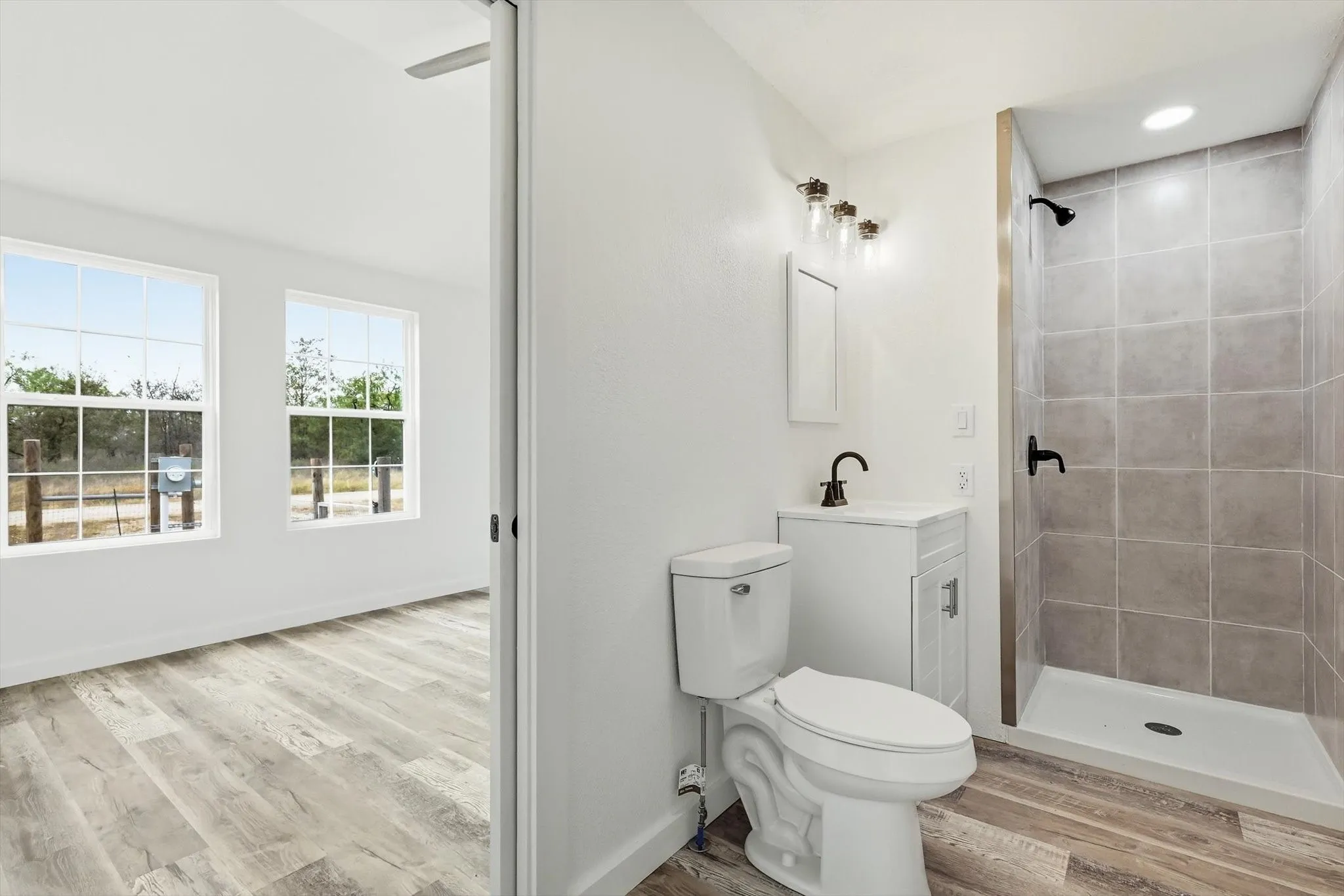 Full bathroom featuring a walk-in shower with tile surround, a single vanity with storage, and wood-finish flooring