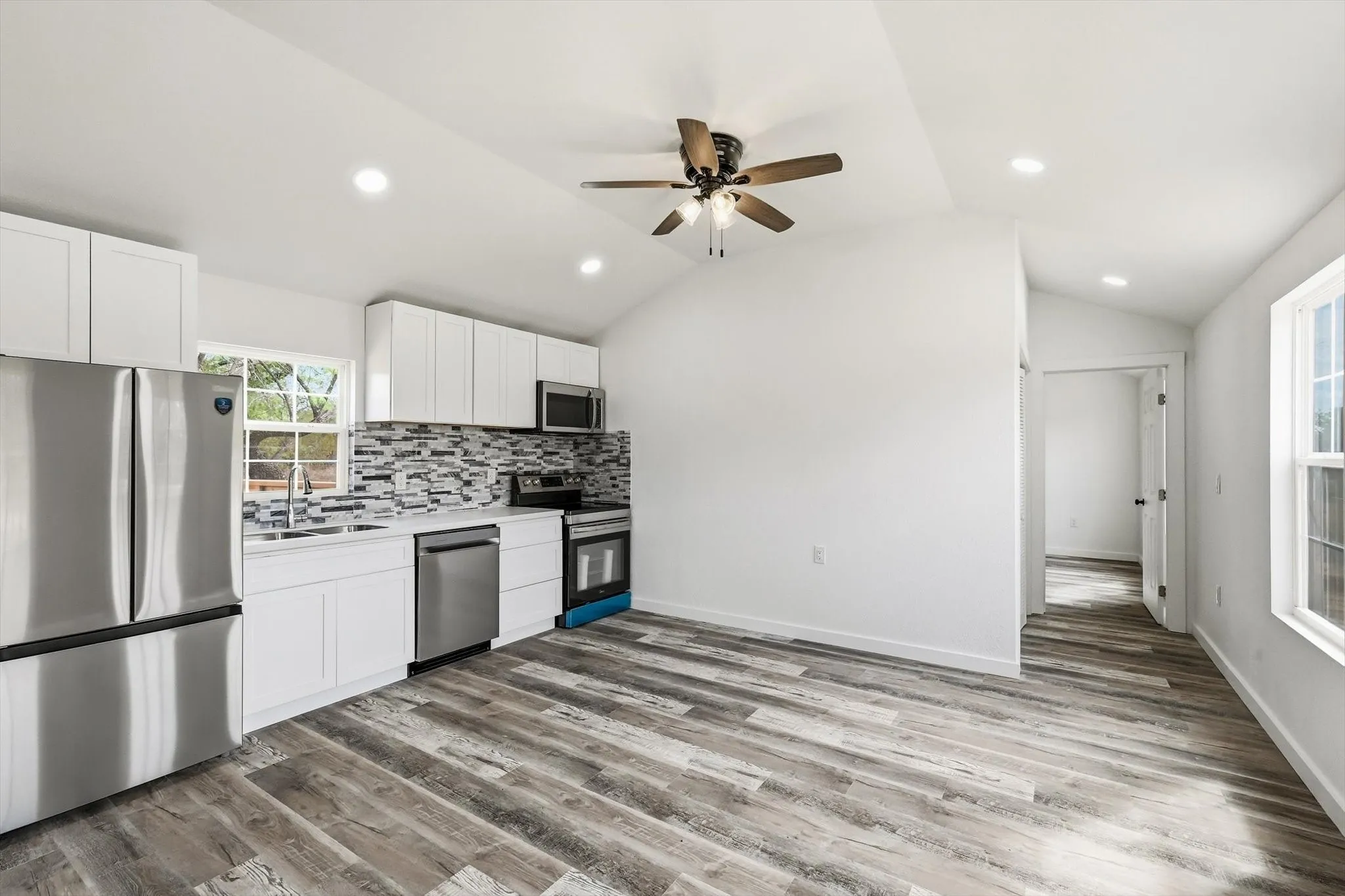 Open-concept kitchen with stainless steel appliances, white cabinetry, a decorative tile backsplash, and wood-finish flooring