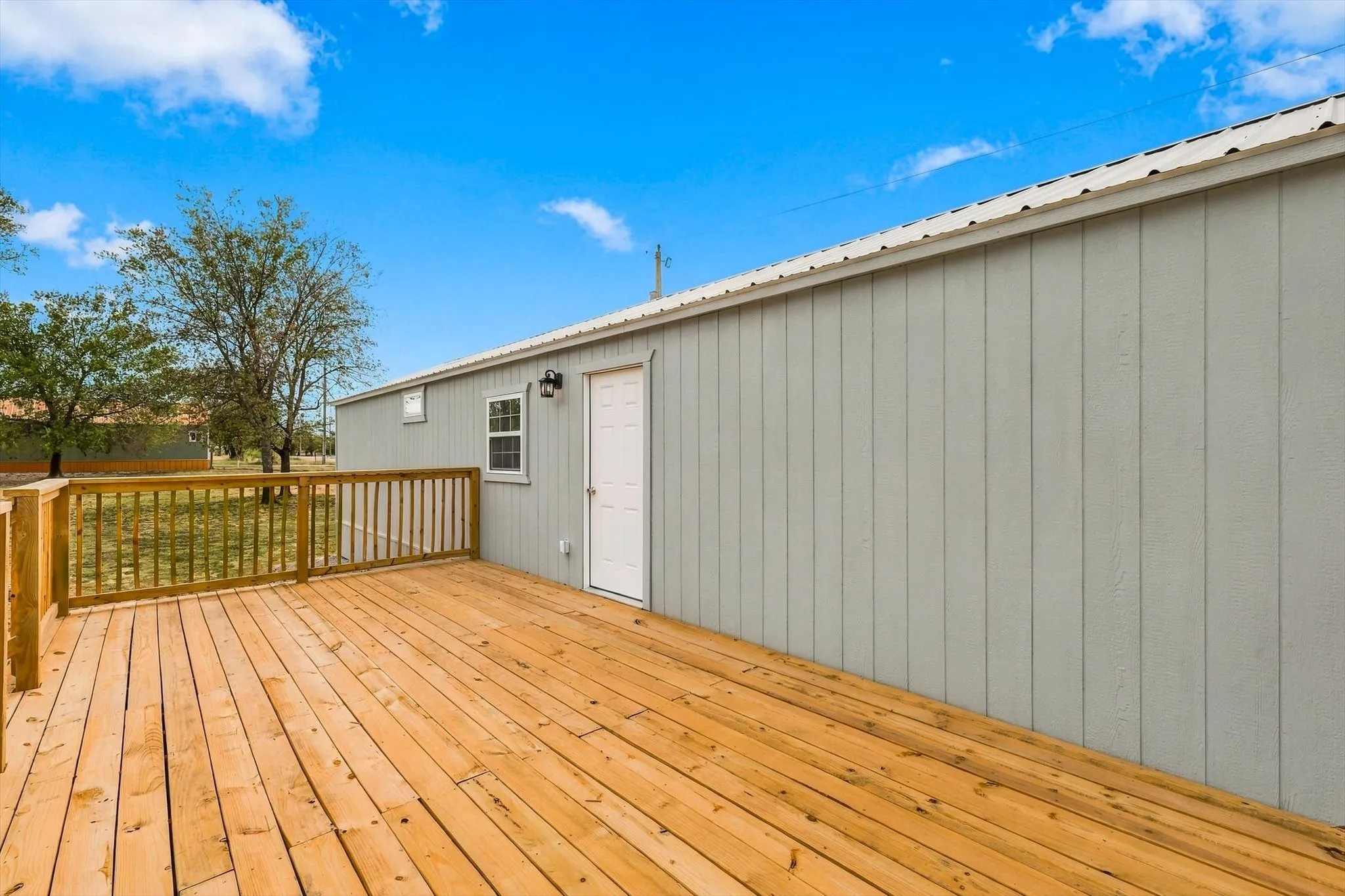 Expansive wood deck with wood railing, light gray vertical siding, white door, and exterior lighting fixture