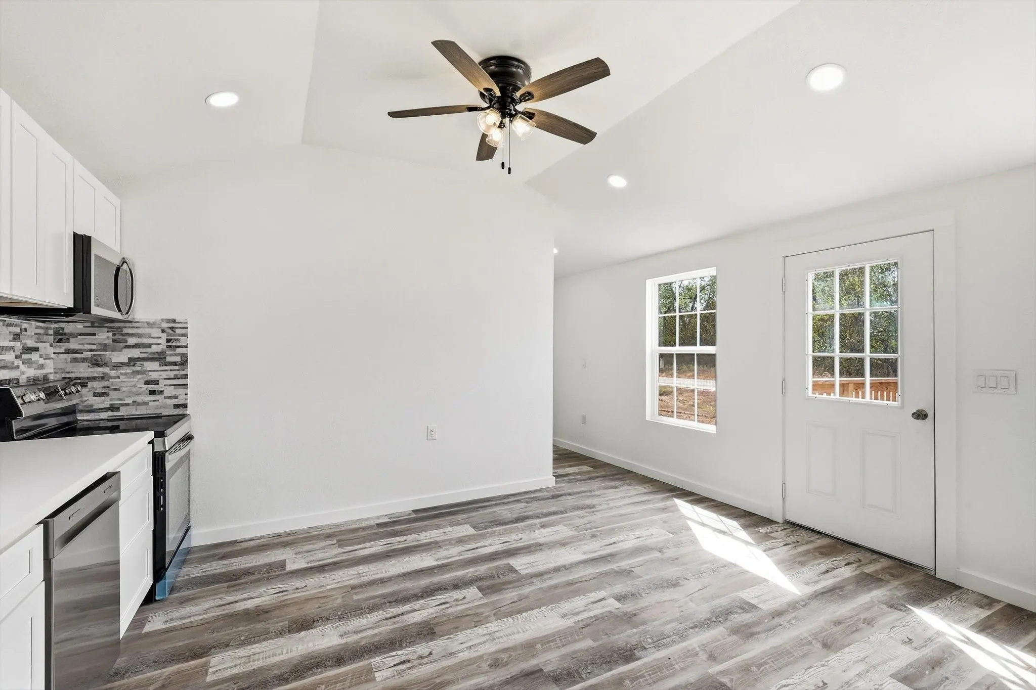Vaulted ceiling with recessed lighting, wood-finish flooring, white cabinetry, stainless steel appliances, and a tiled backsplash