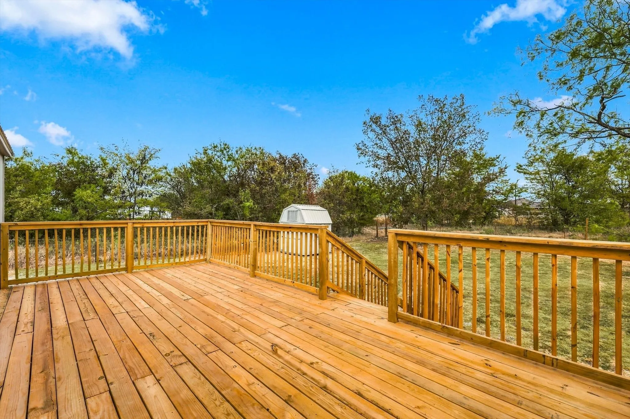 Expansive wood-plank deck with wood railings, featuring steps to a grassy area, and perimeter trees