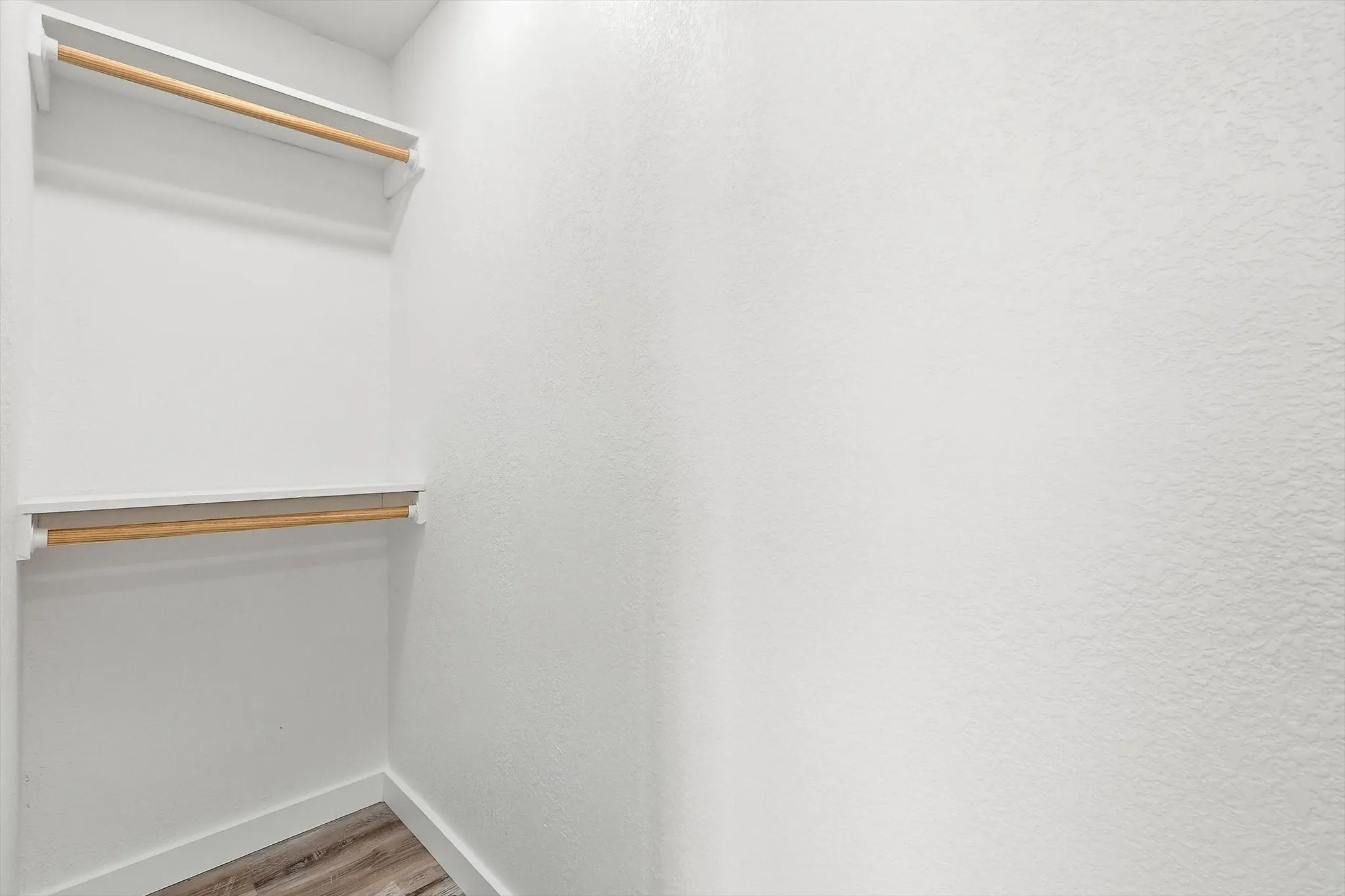 White walls, wood-finish flooring, and two wood hanging rods