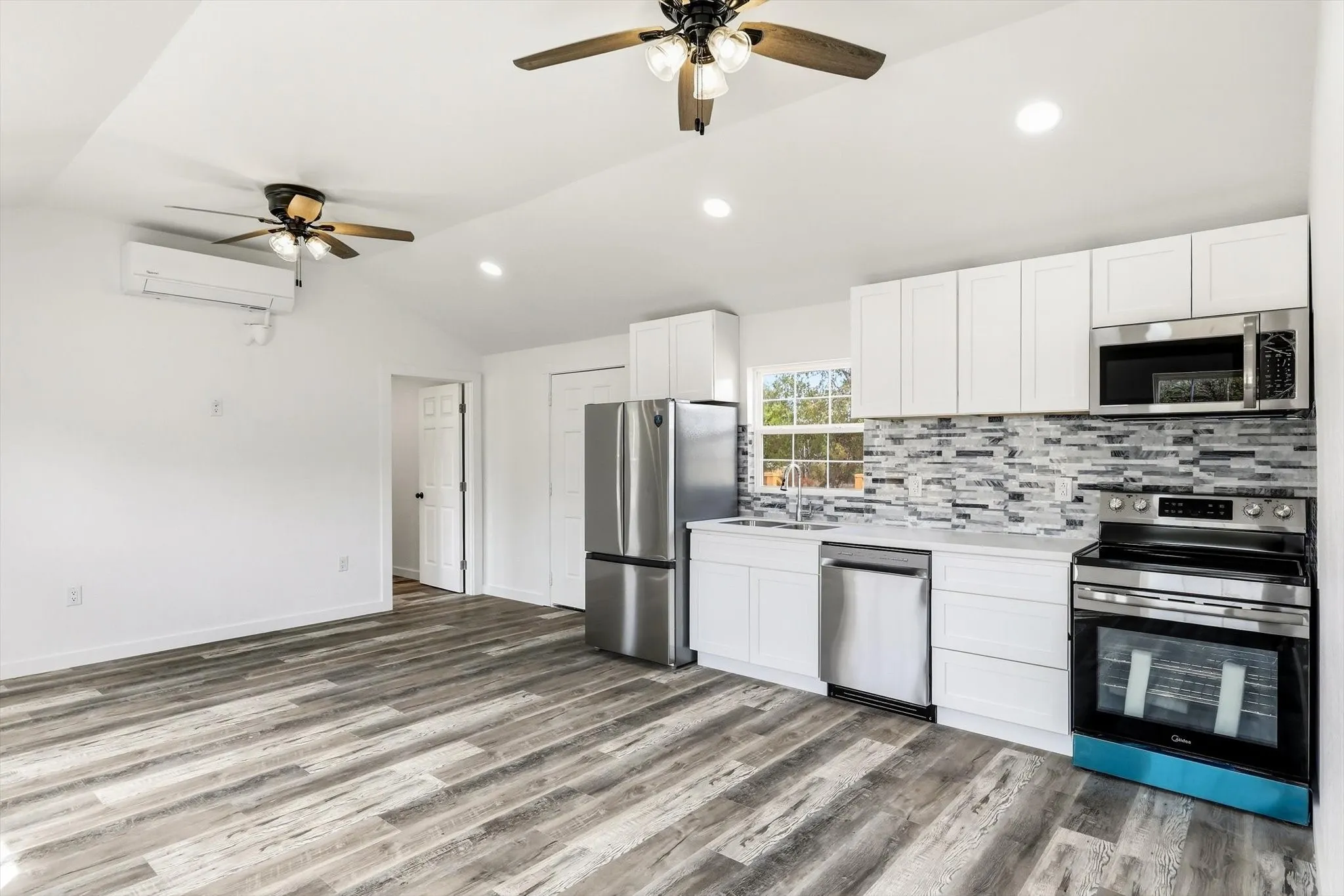 Kitchen featuring stainless steel appliances, white cabinetry, and a textured tile backsplash