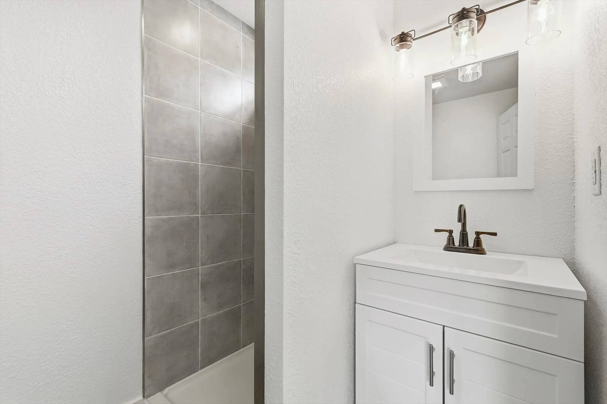 White vanity with an integrated sink, bronze-finish faucet, and coordinating bronze-finish light fixture
