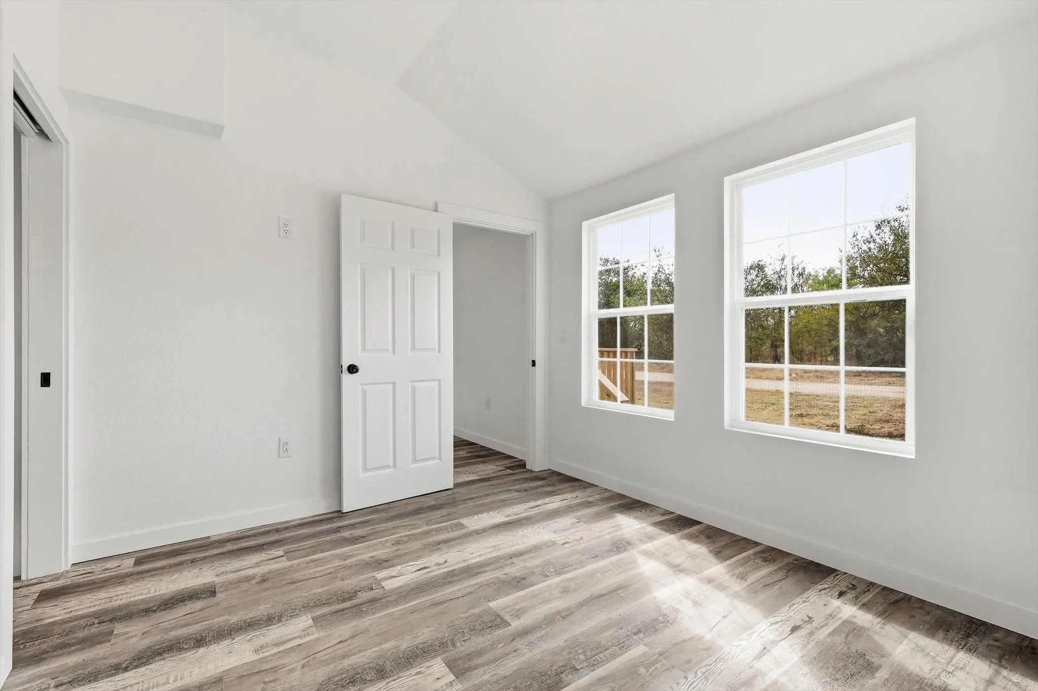 Vaulted ceiling with a white finish, two double-hung windows, and wood-finish flooring
