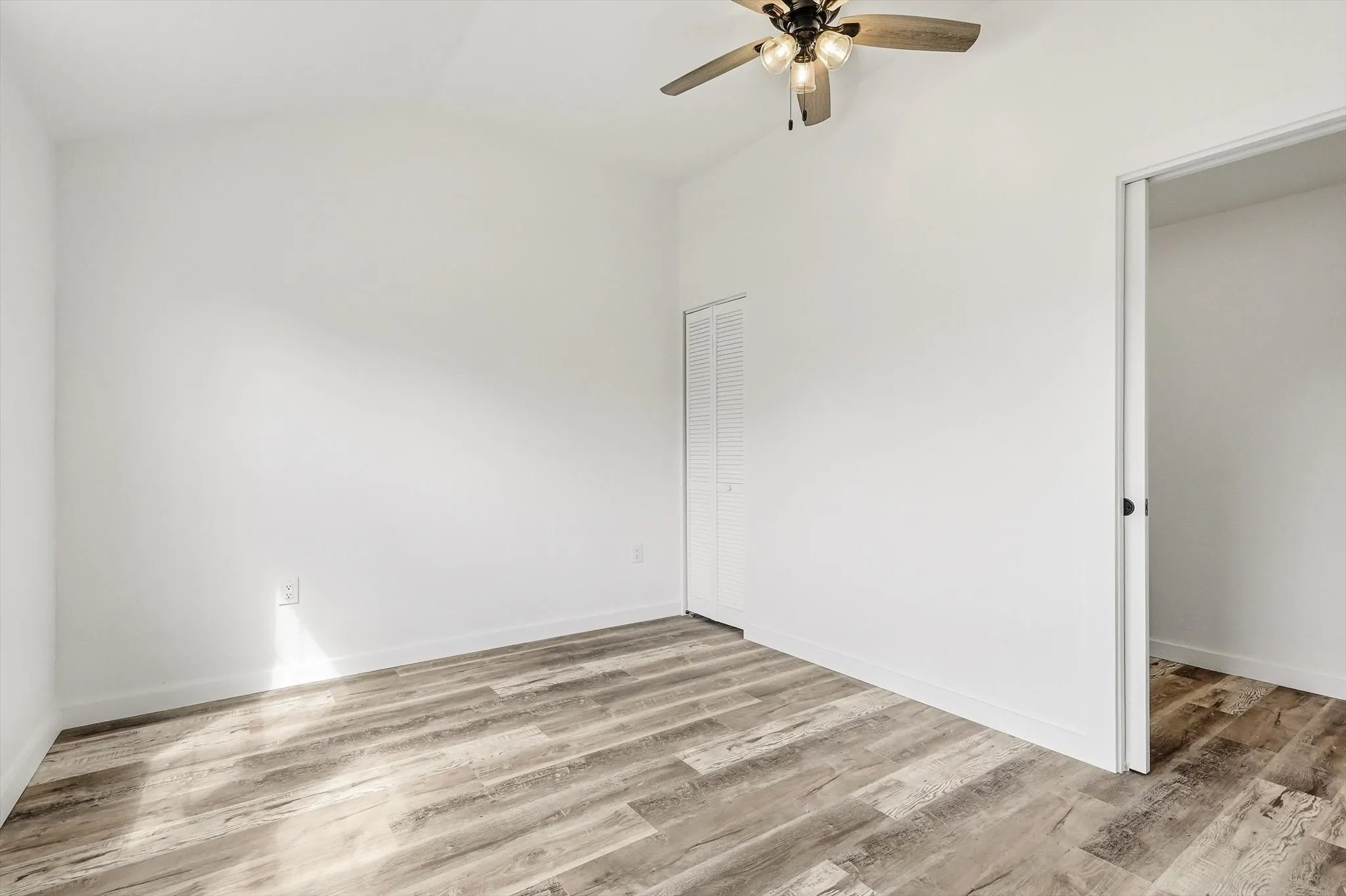Vaulted ceiling with a ceiling fan, wood-finish flooring, and a bifold closet door