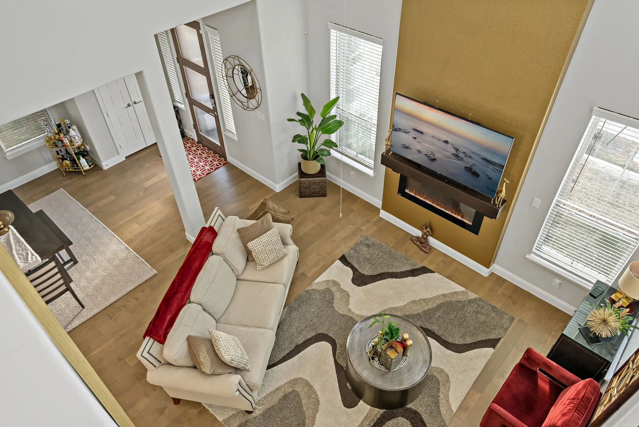 Open-concept living area featuring a two-story accent wall with an integrated electric fireplace, wood-finish flooring, and multiple windows