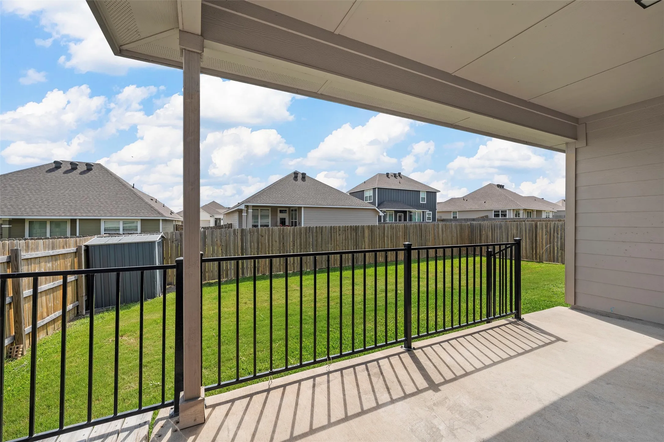 Fenced backyard featuring a residential view, a storage unit, and a patio area