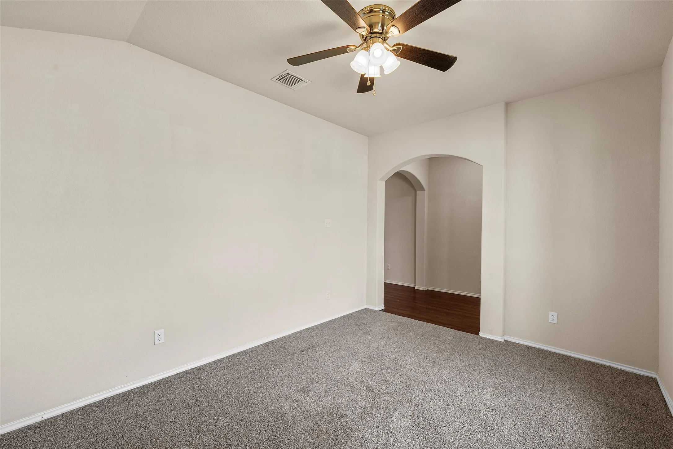 Unfurnished room with dark colored carpet, arched walkways, and a ceiling fan