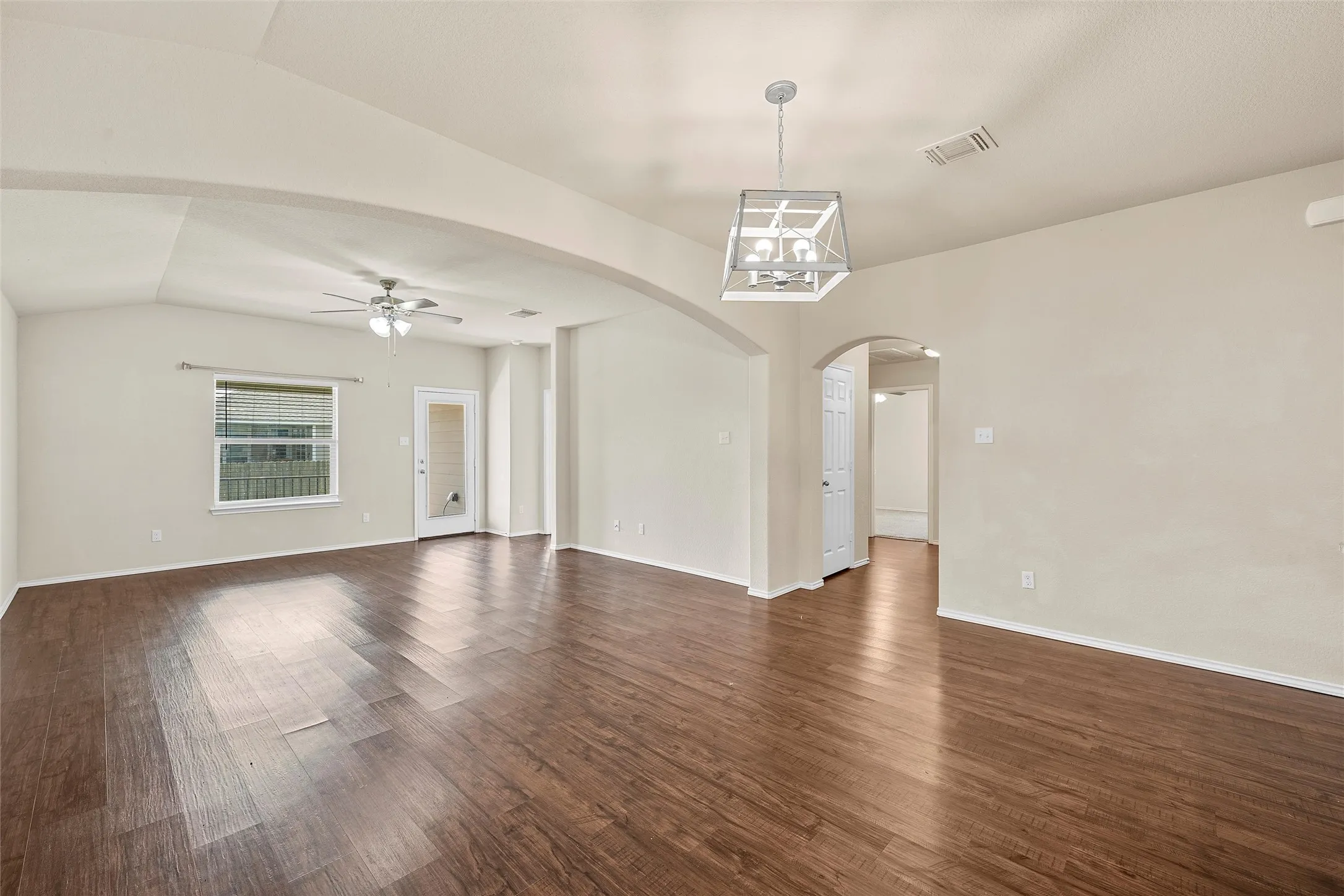 Spare room featuring lofted ceiling, a ceiling fan, arched walkways, dark wood-style floors, and a chandelier