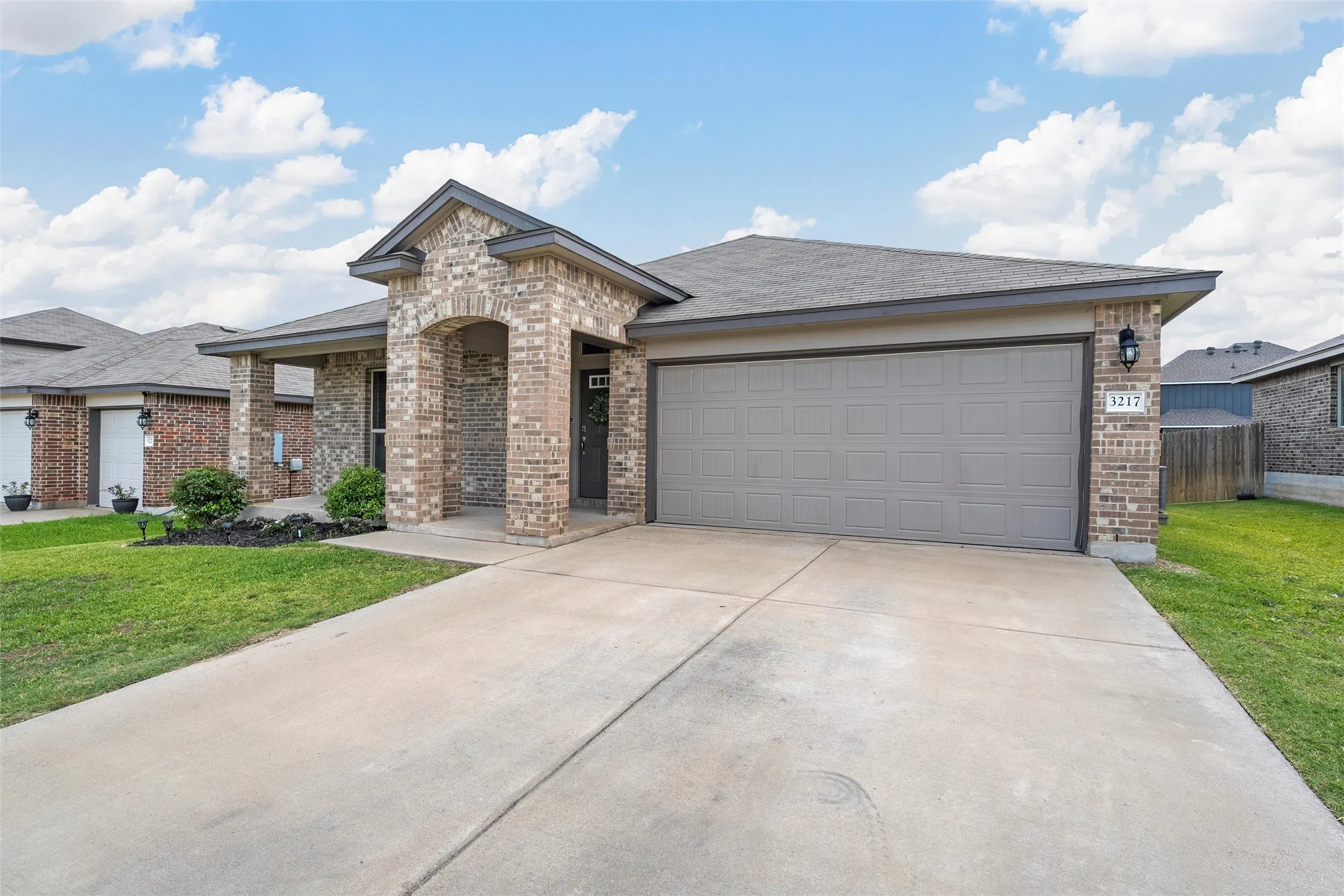 View of front of property with brick siding, driveway, an attached garage, and roof with shingles