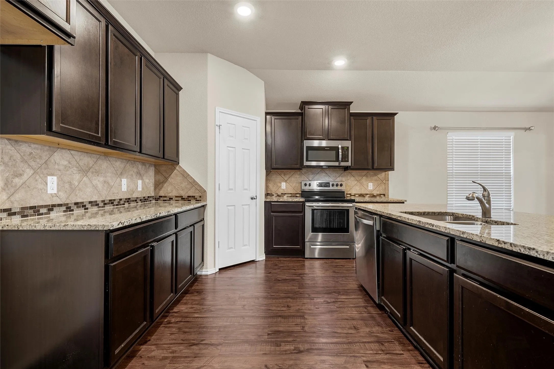 Kitchen with stainless steel appliances, light stone countertops, dark brown cabinets, dark wood-type flooring, and recessed lighting
