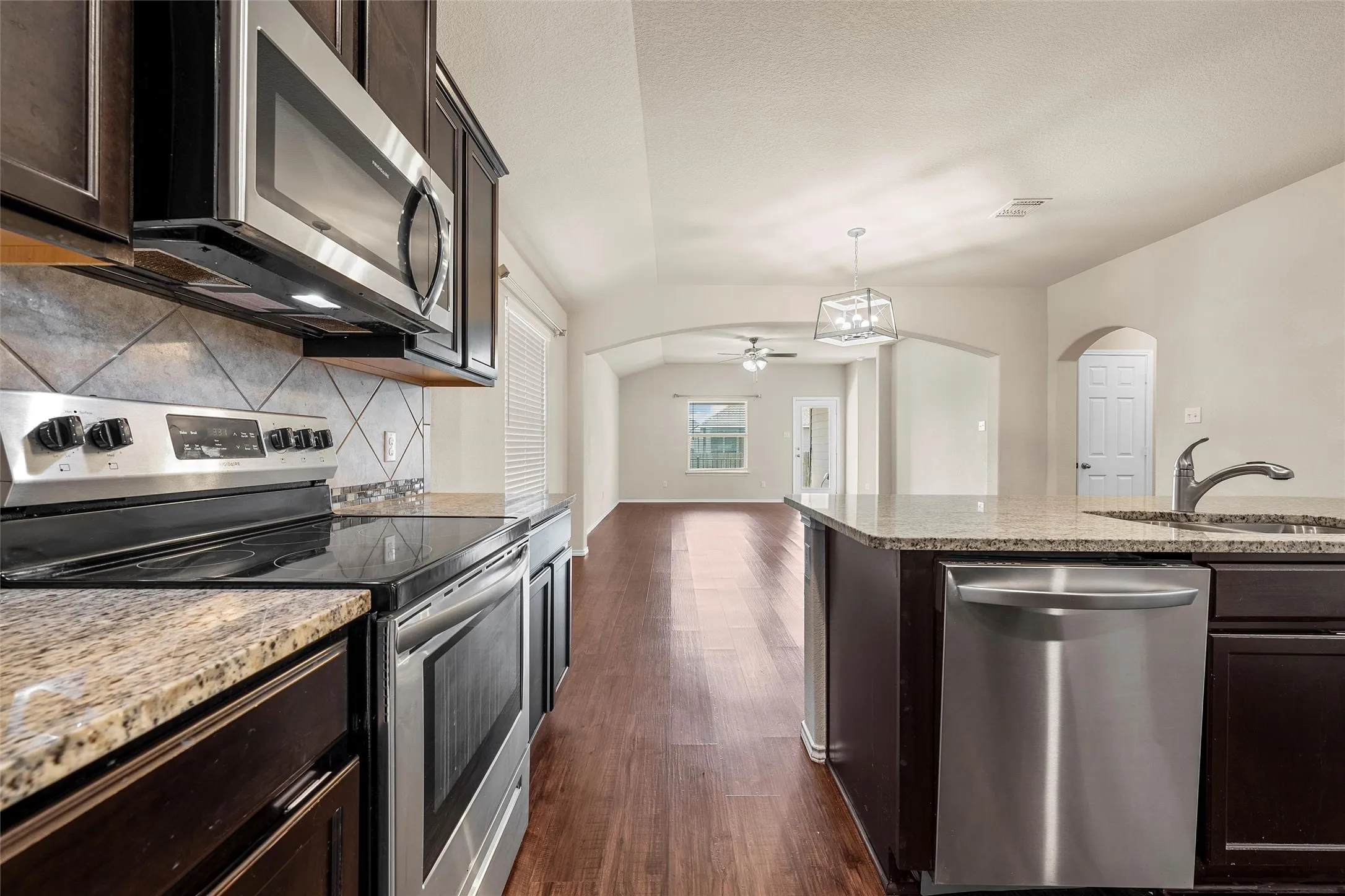 Kitchen with stainless steel appliances, arched walkways, decorative backsplash, dark wood-type flooring, and ceiling fan