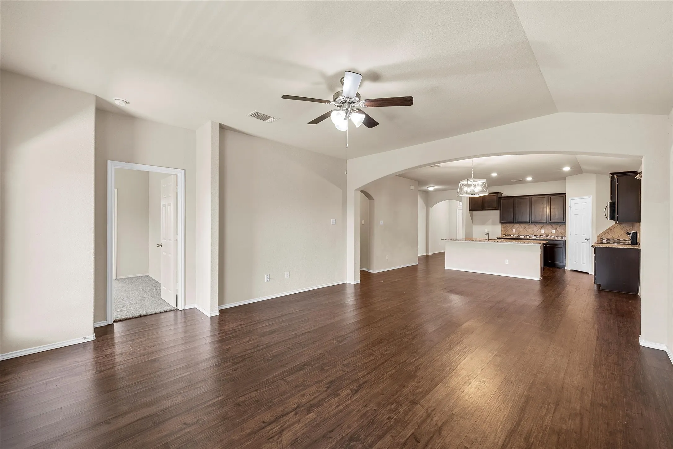 Unfurnished living room with arched walkways, ceiling fan, and dark wood-style floors