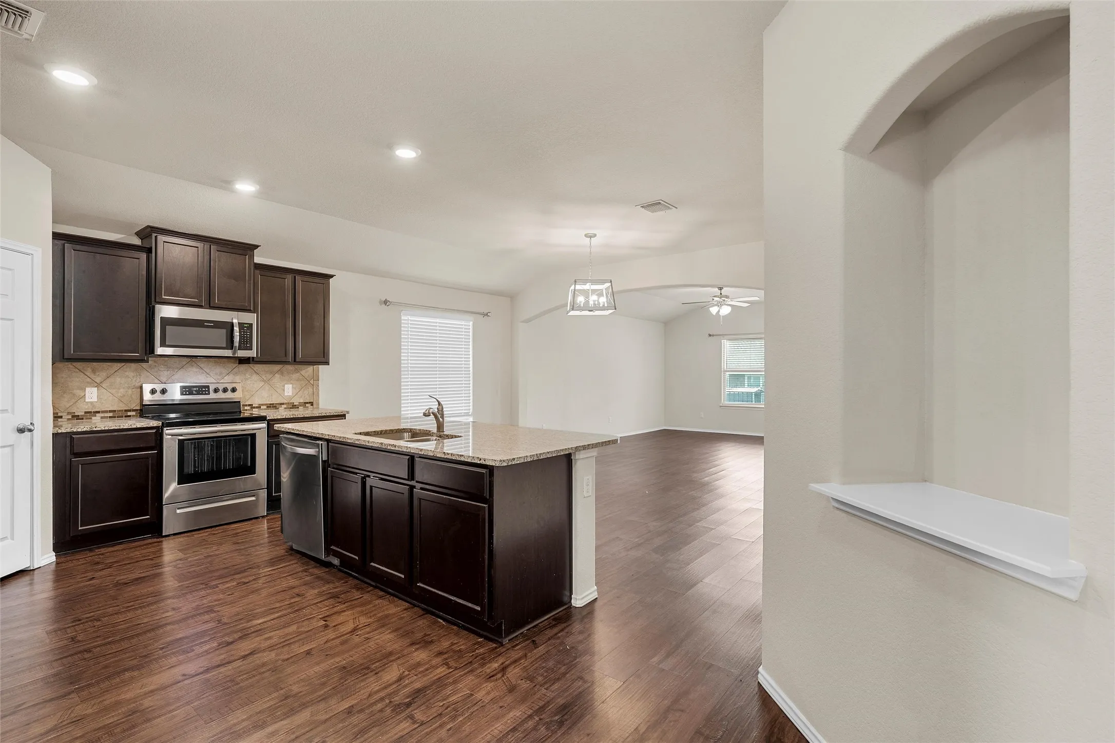 Kitchen with appliances with stainless steel finishes, dark wood-style flooring, decorative backsplash, dark brown cabinets, and light stone countertops