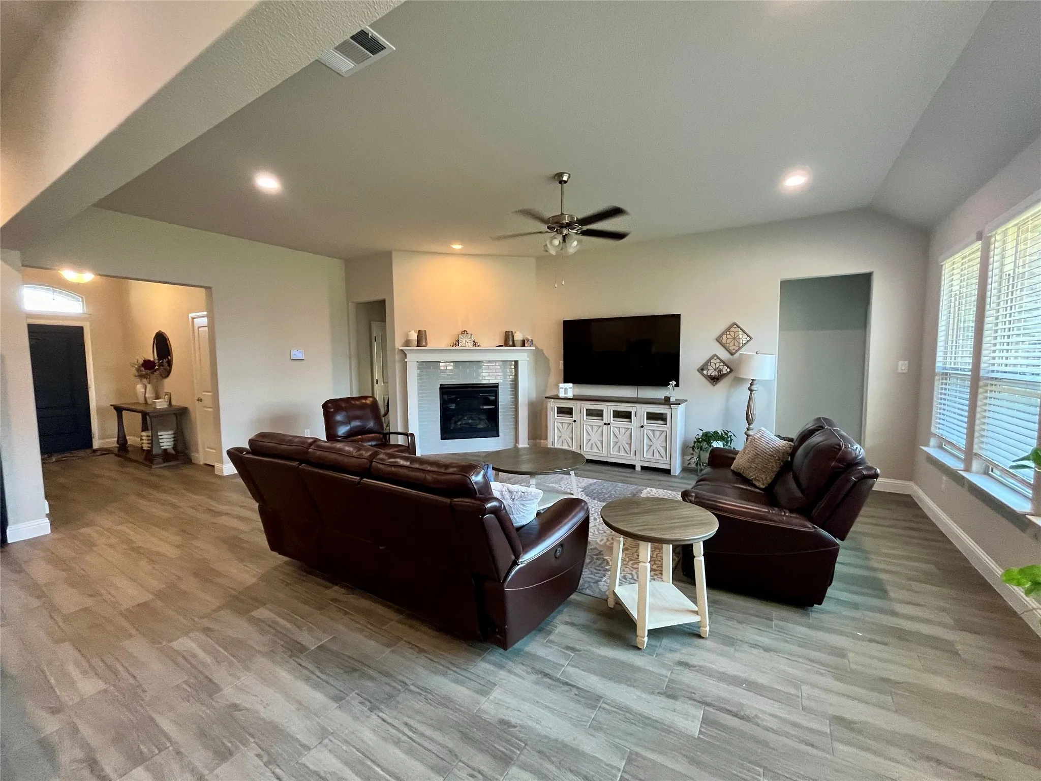 Spacious living area featuring wood-finish flooring, a corner fireplace with a white mantel, recessed lighting, and a ceiling fan