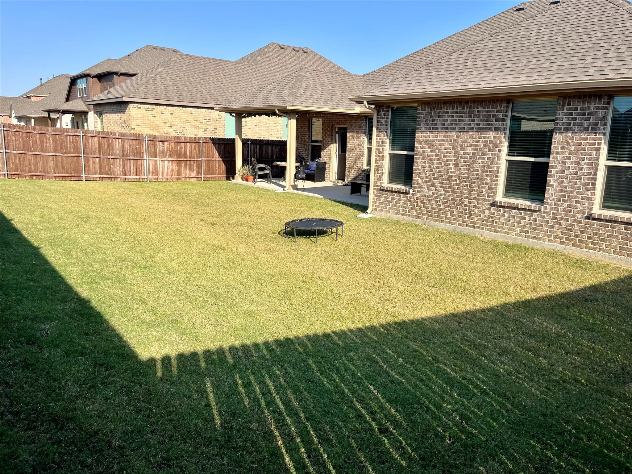 Expansive backyard featuring a manicured lawn, full privacy fencing, and a covered concrete patio