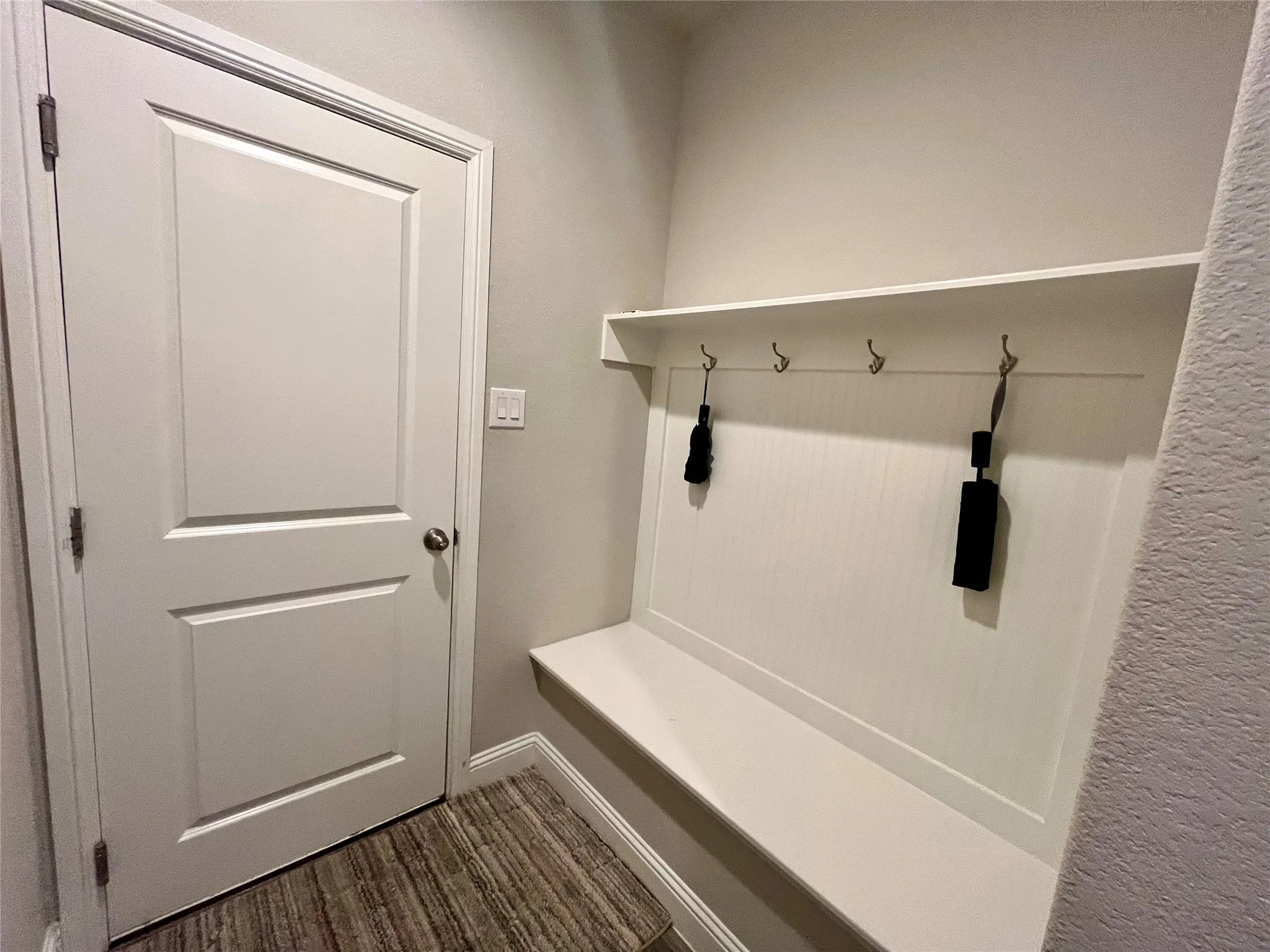 Built-in storage bench with beadboard paneling, wall-mounted hooks, and overhead shelving