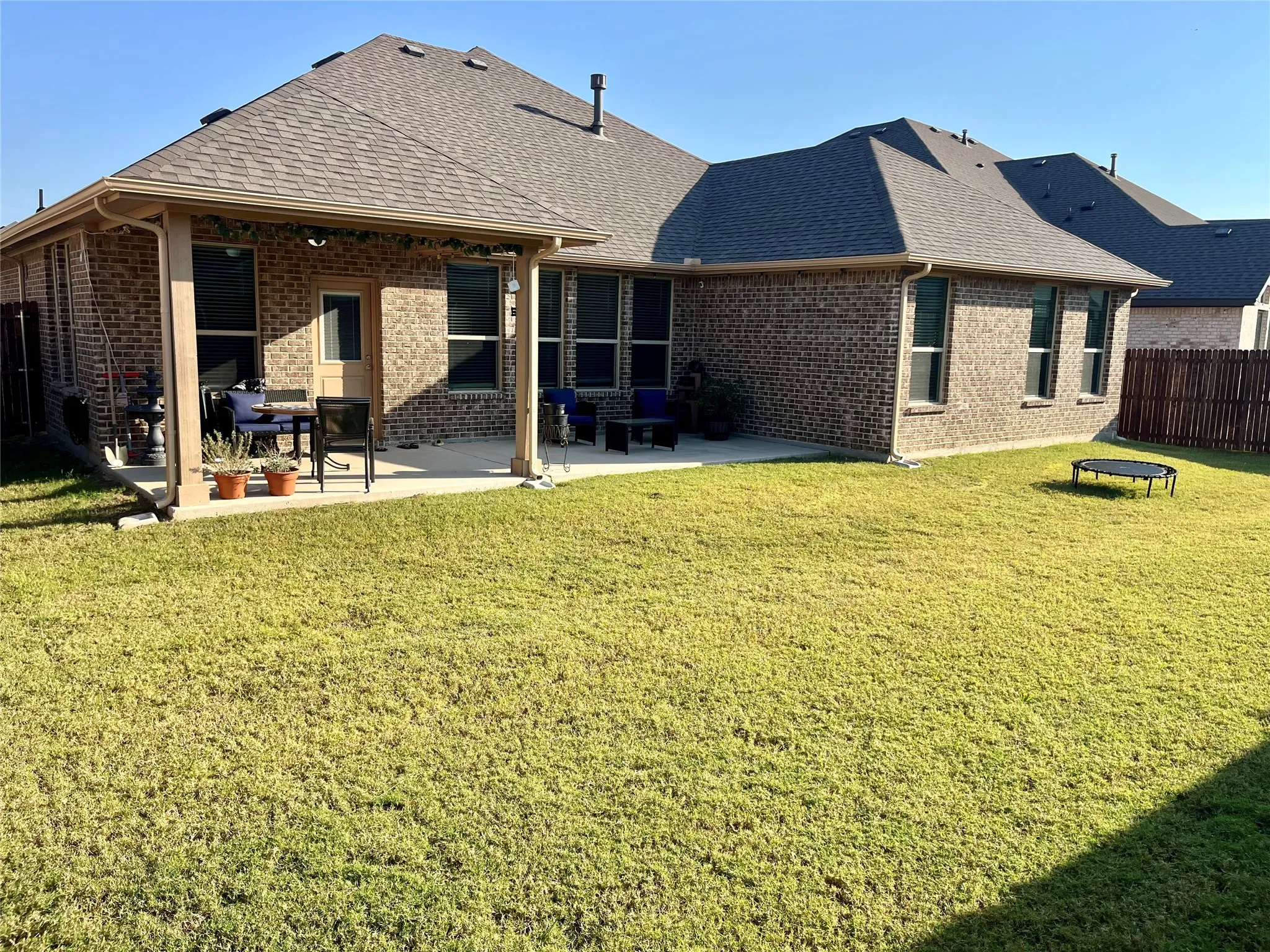 Expansive backyard with a covered patio, brick exterior, and a fenced perimeter