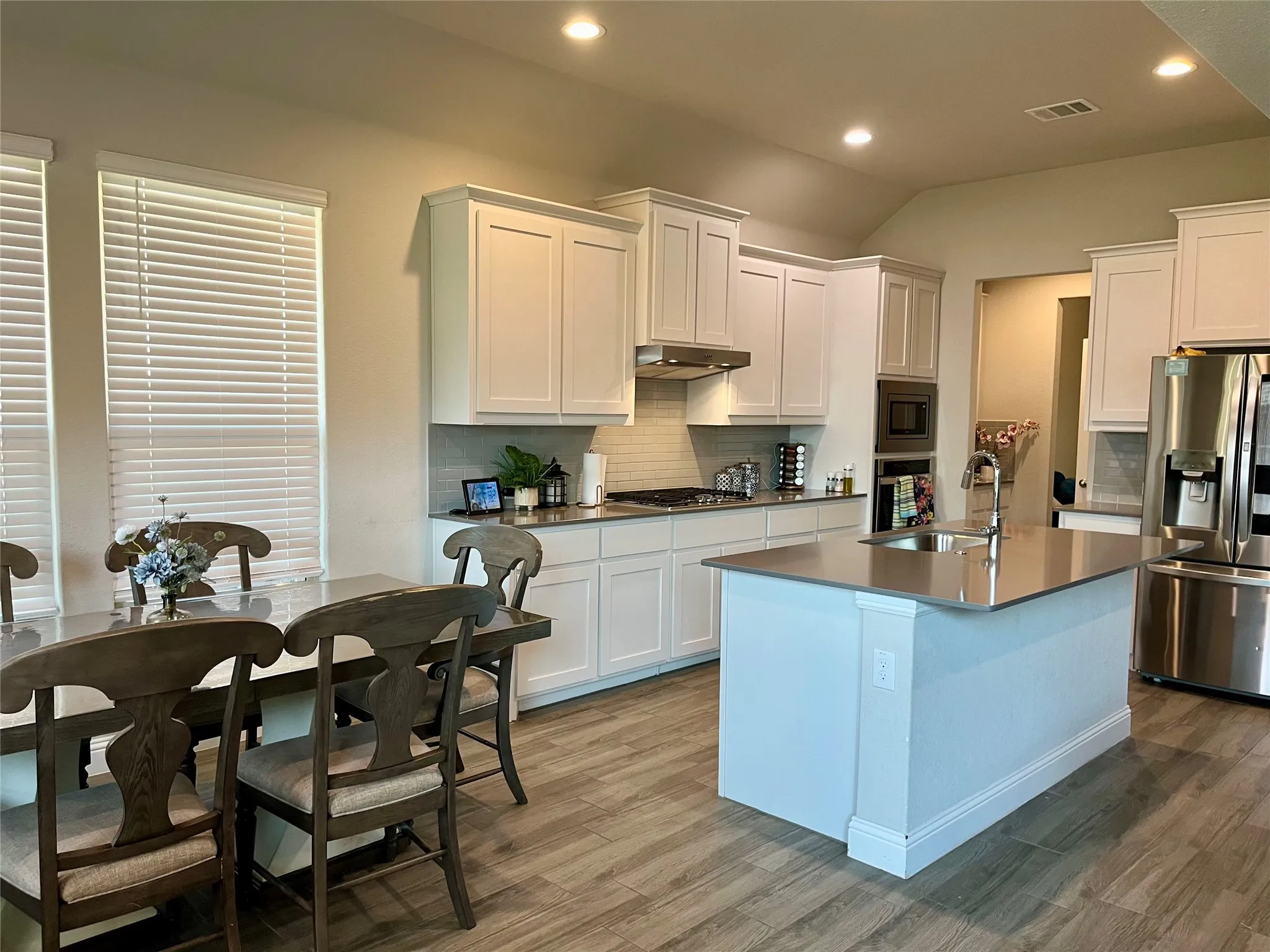 Open-concept kitchen with white shaker-style cabinetry, recessed lighting, wood-finish flooring, and a central island with an integrated sink
