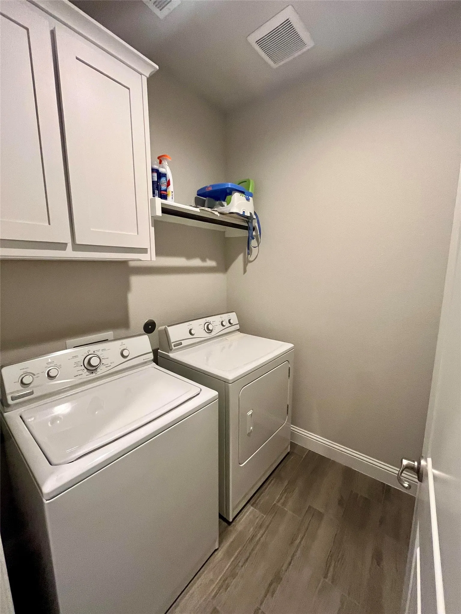 Laundry area featuring wood-look tile flooring, white shaker-style cabinetry, and a ceiling-mounted ventilation system