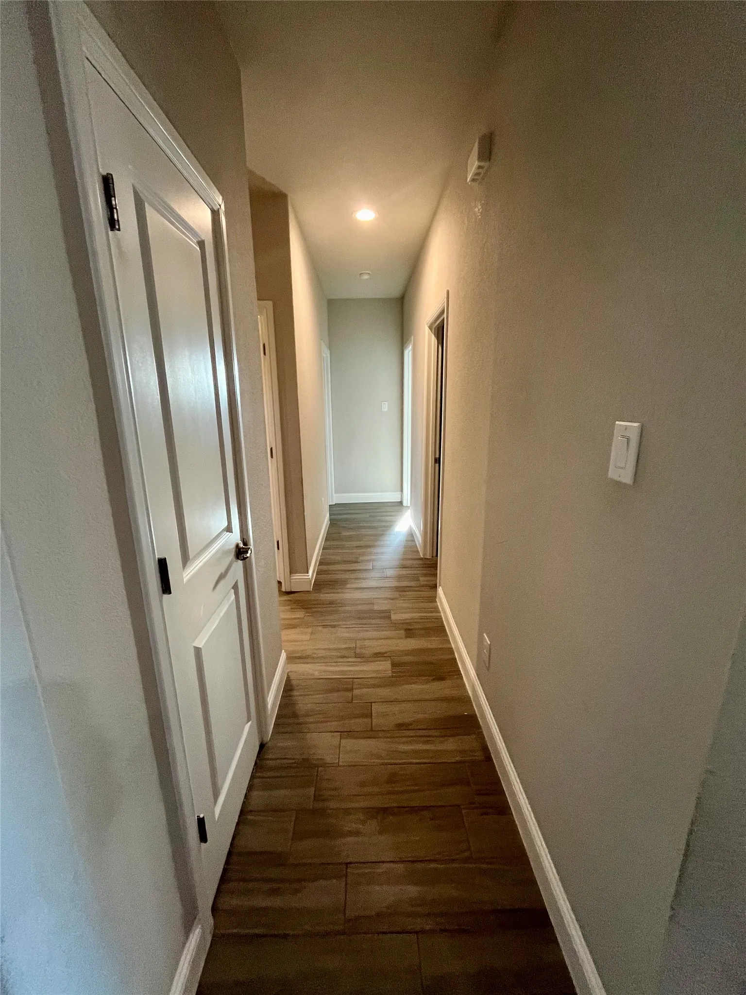 Hallway featuring wood-finish flooring, white six-panel doors, neutral wall finishes, and recessed lighting throughout