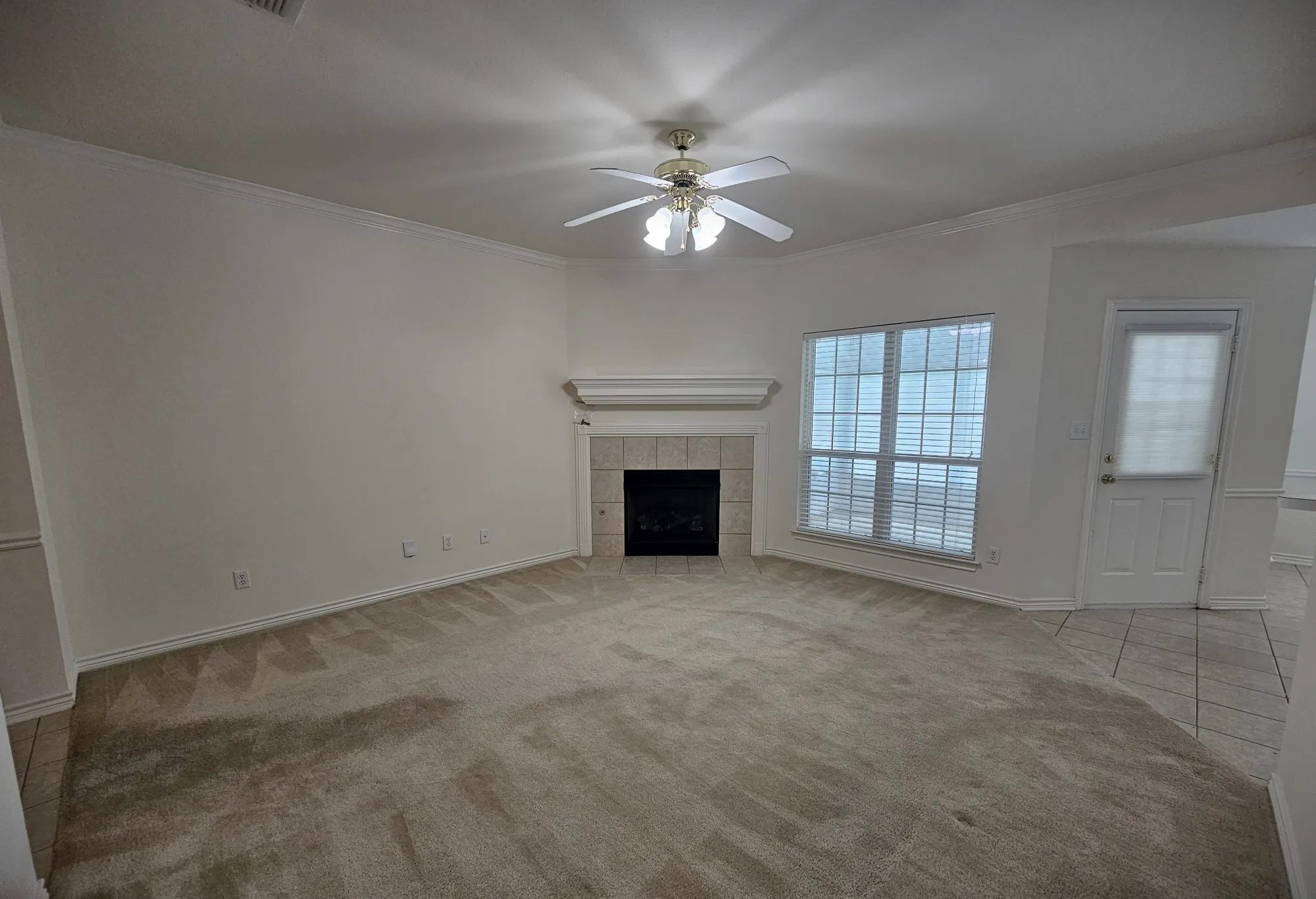 Spacious living area featuring a fireplace with a tile surround and mantel, a ceiling fan with integrated lighting, and multiple windows