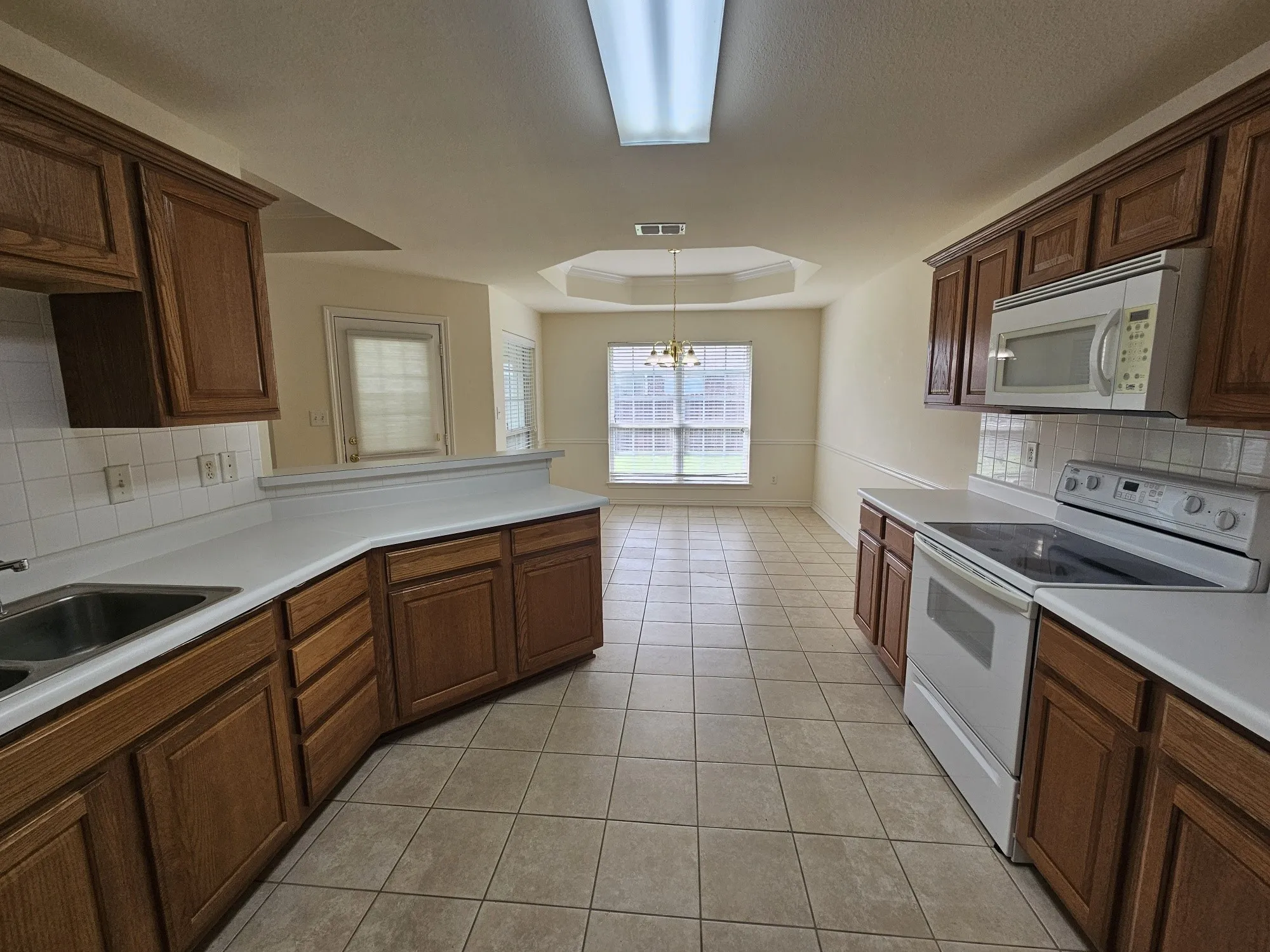 Tile flooring throughout, tray ceiling with crown molding, chair rail molding, wood cabinetry, and white appliances