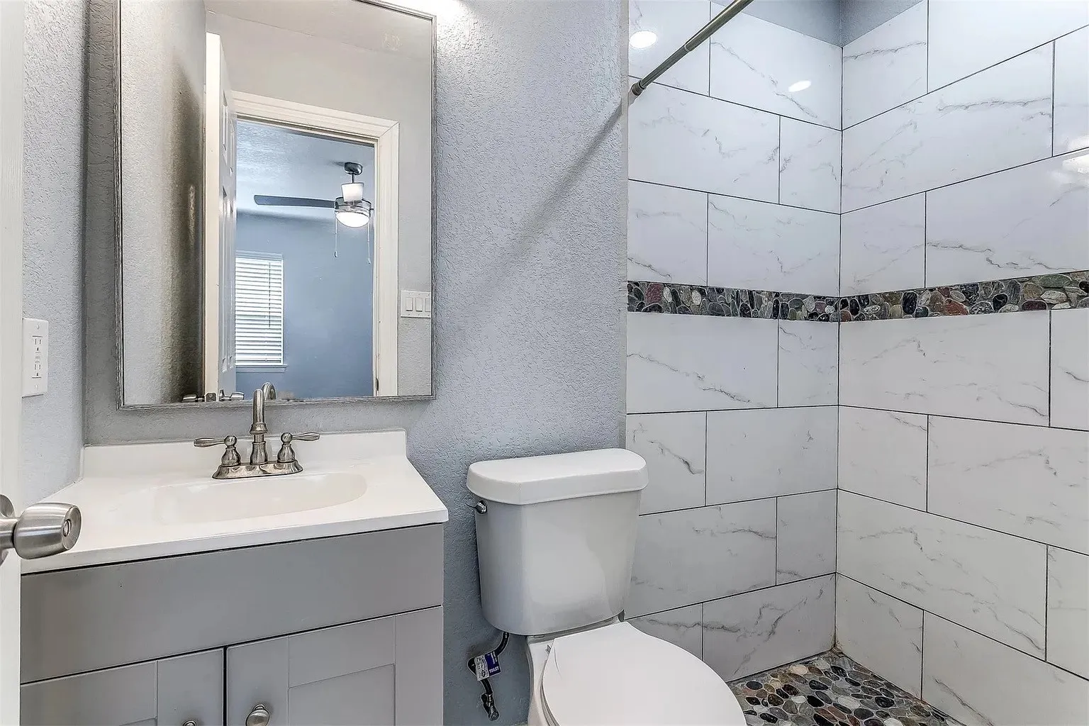 Vanity with integrated sink, white tiled shower surround with pebble accent, and pebble shower floor