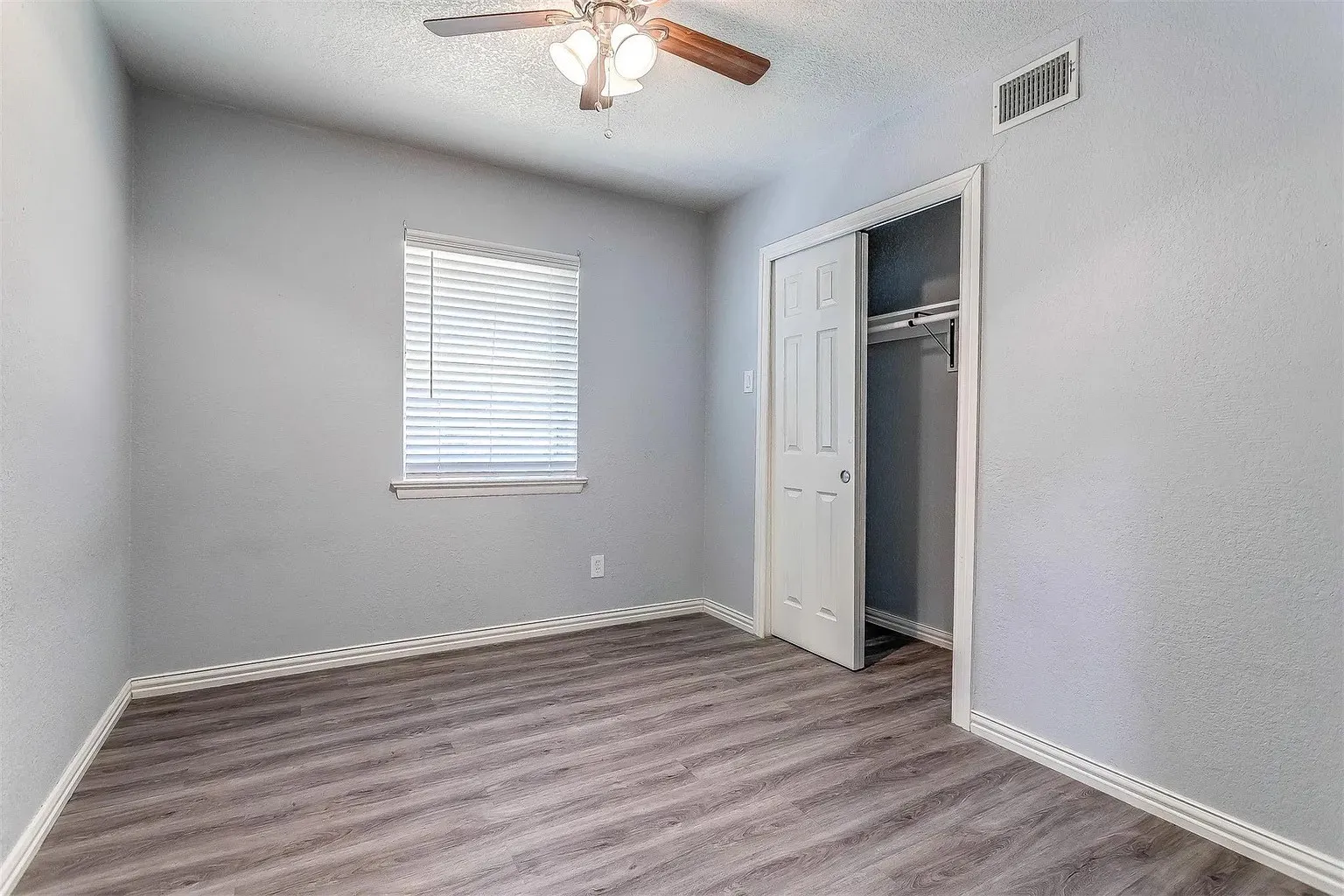 Wood-finish flooring, ceiling fan with integrated lighting, window with blinds, and a built-in closet with sliding doors