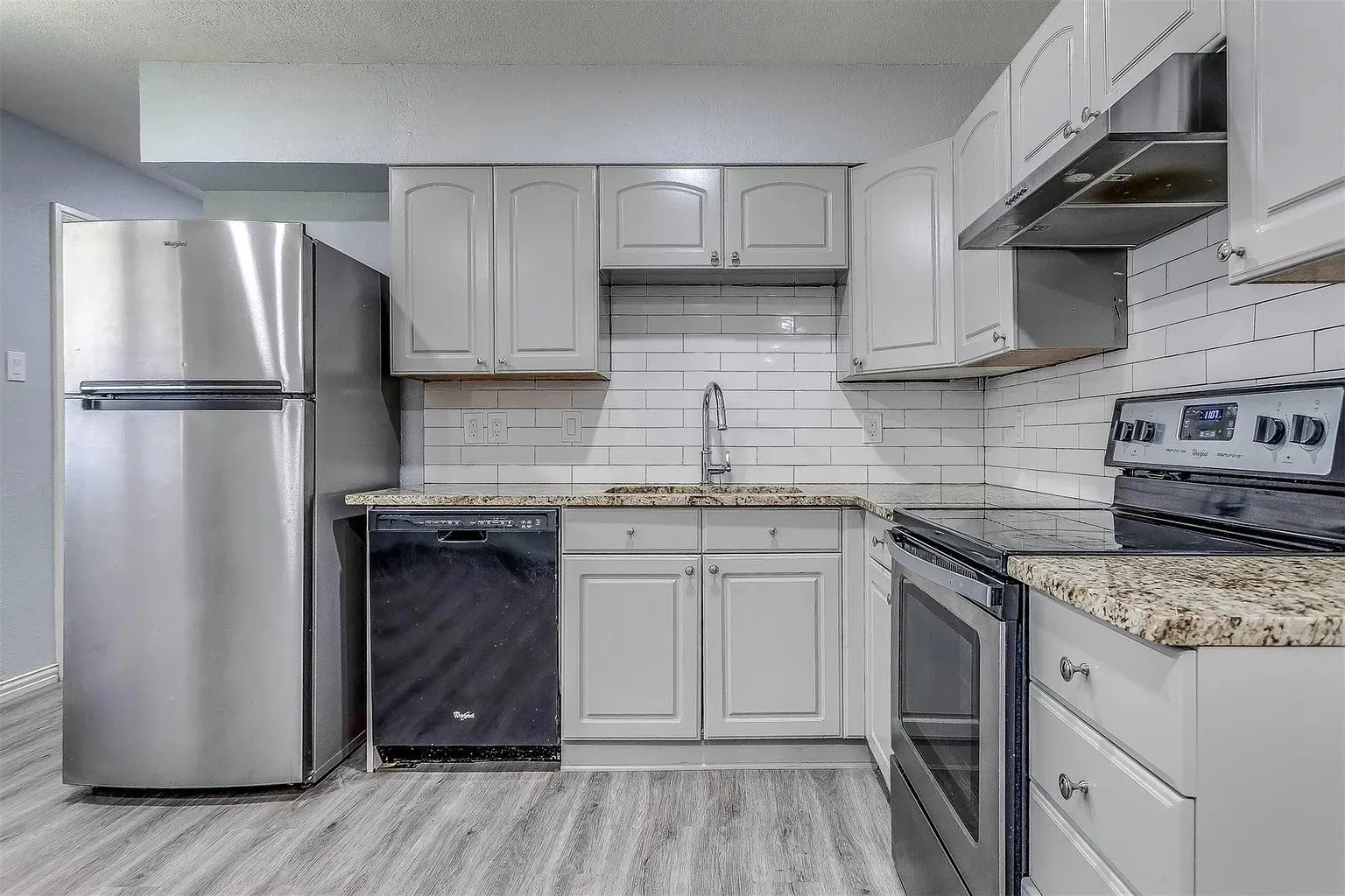 Kitchen featuring light-toned cabinetry, granite-style countertops, subway tile backsplash, stainless steel appliances, and wood-finish flooring