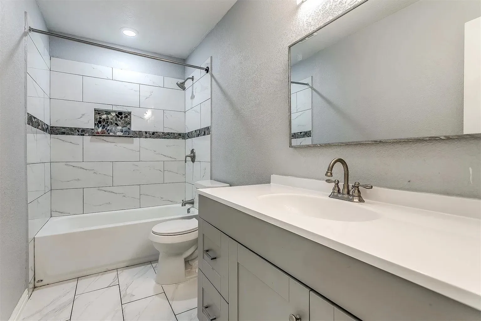 Bathroom featuring a vanity with an integrated sink, a rectangular mirror, a bathtub with a shower, a tiled surround, and a recessed shower niche