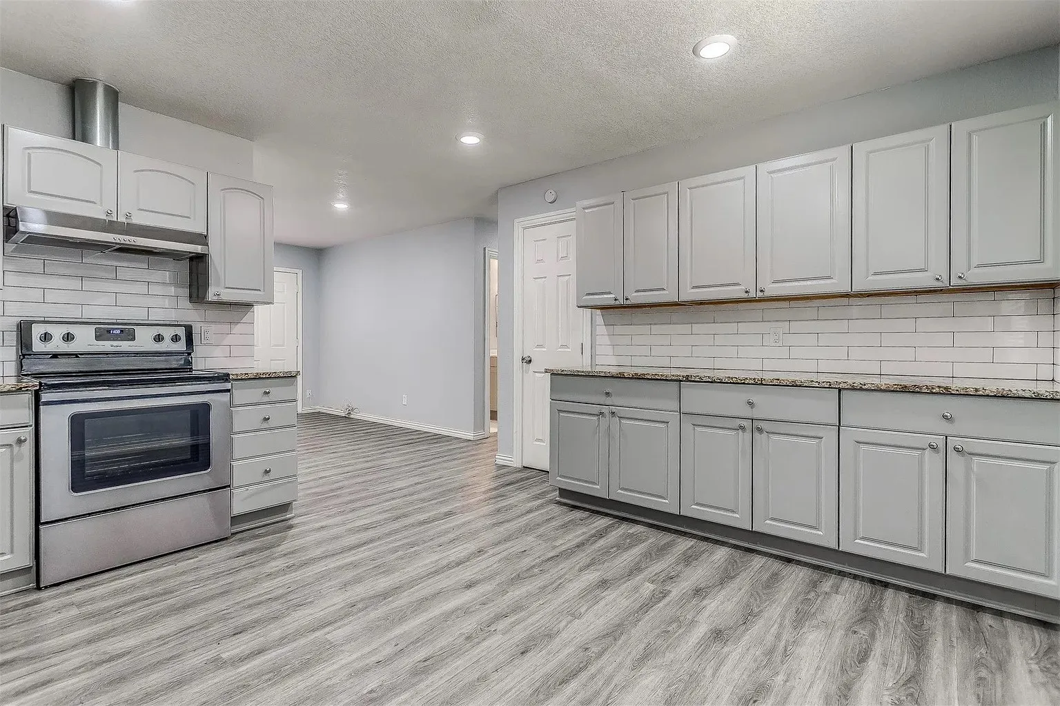 Kitchen featuring wood-finish flooring, light gray cabinetry, stainless steel oven with range hood, white subway tile backsplash, and recessed lighting