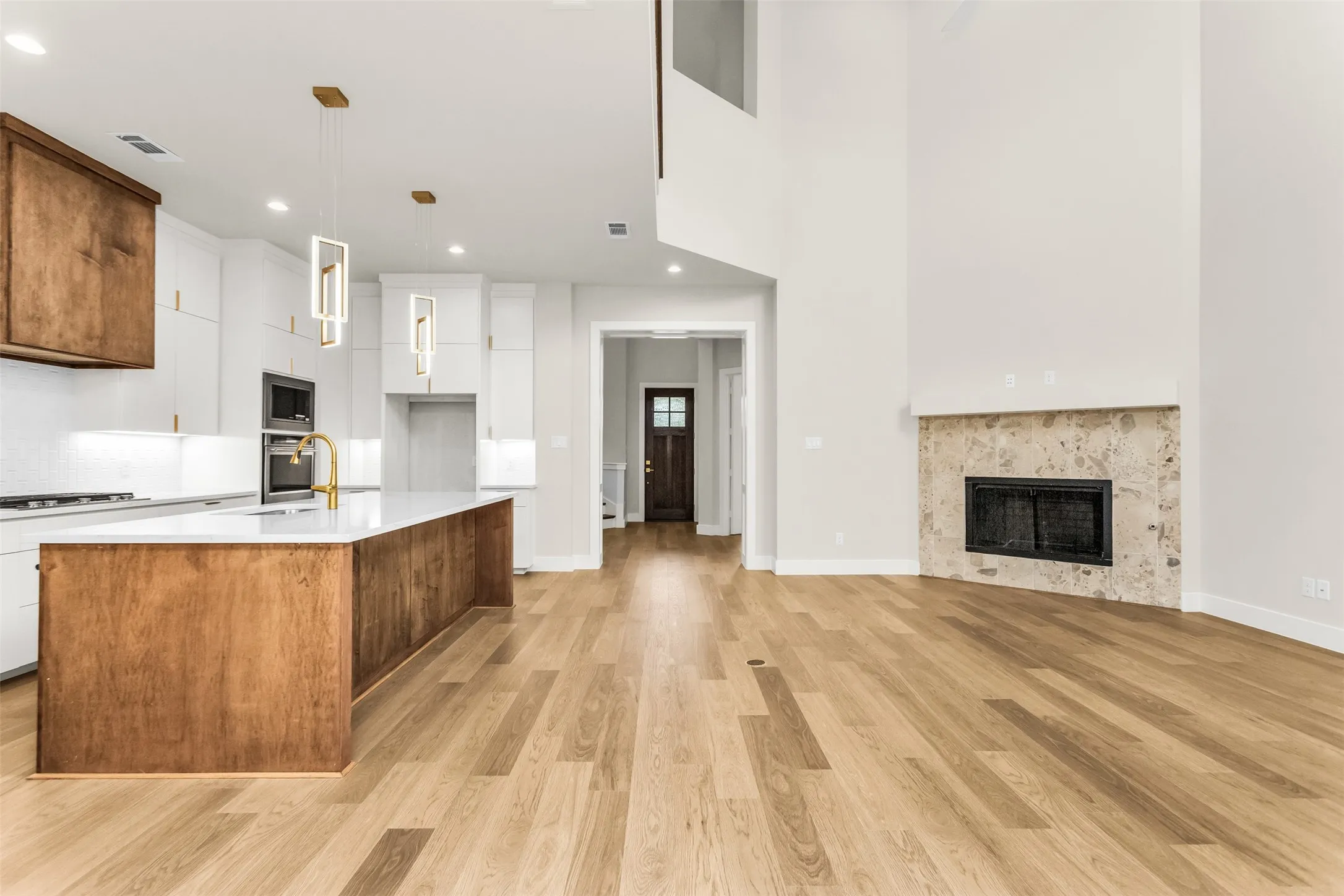 Open-concept living space with wood-finish flooring, a contemporary kitchen island, white cabinetry, a built-in oven, and a natural stone fireplace surround